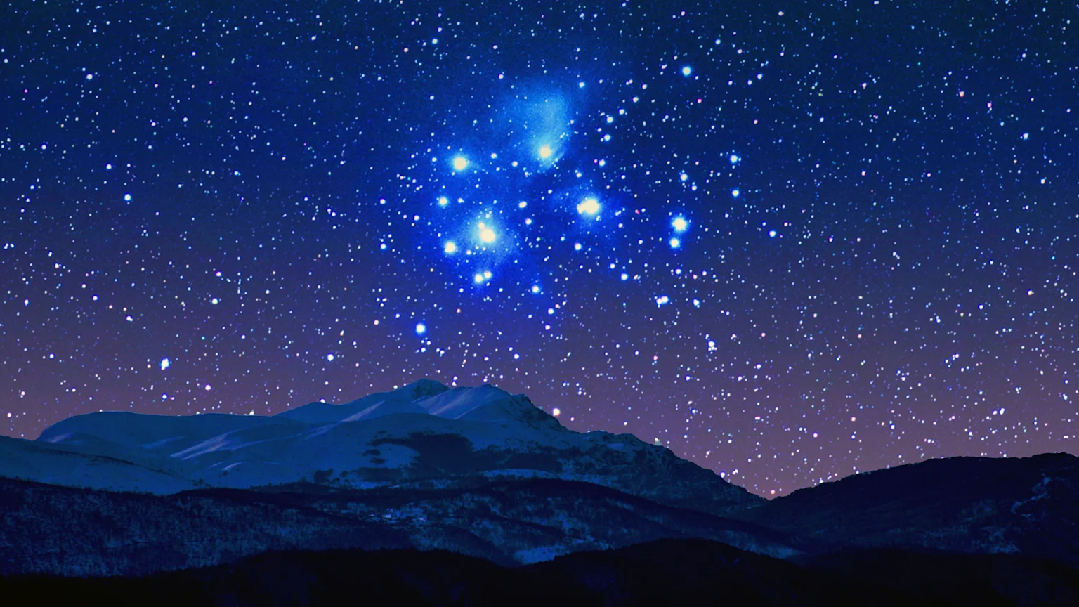 A starry night sky over snow-capped mountains and dark land, featuring a bright blue star cluster (Matariki/Pleiades) in the upper center.