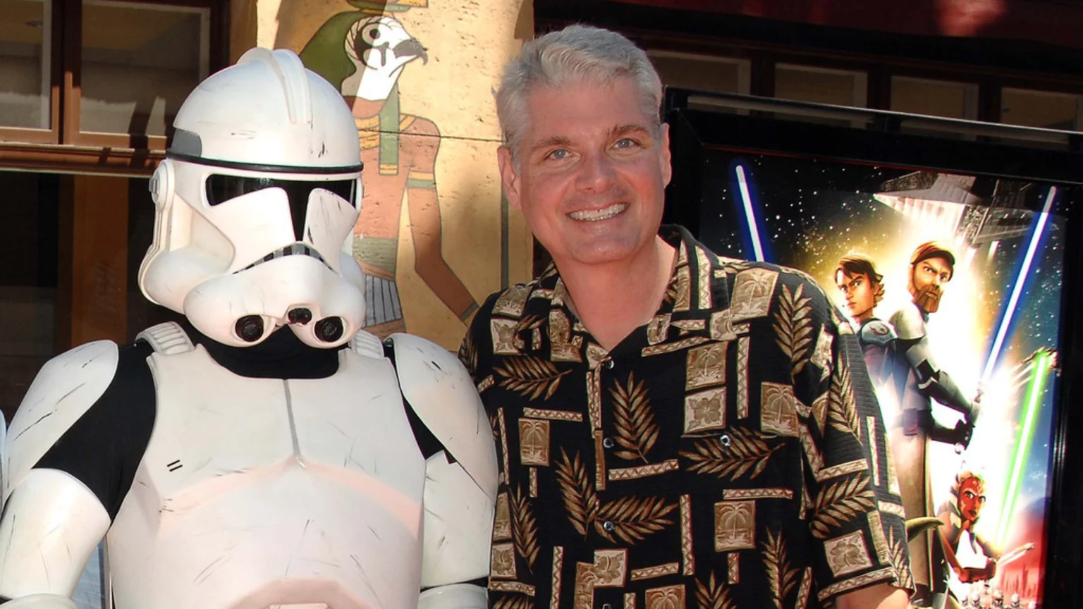 Smiling Tom Kane stands next to a Clone Trooper costume, with a Star Wars: The Clone Wars poster and Egyptian-style wall art in the background.