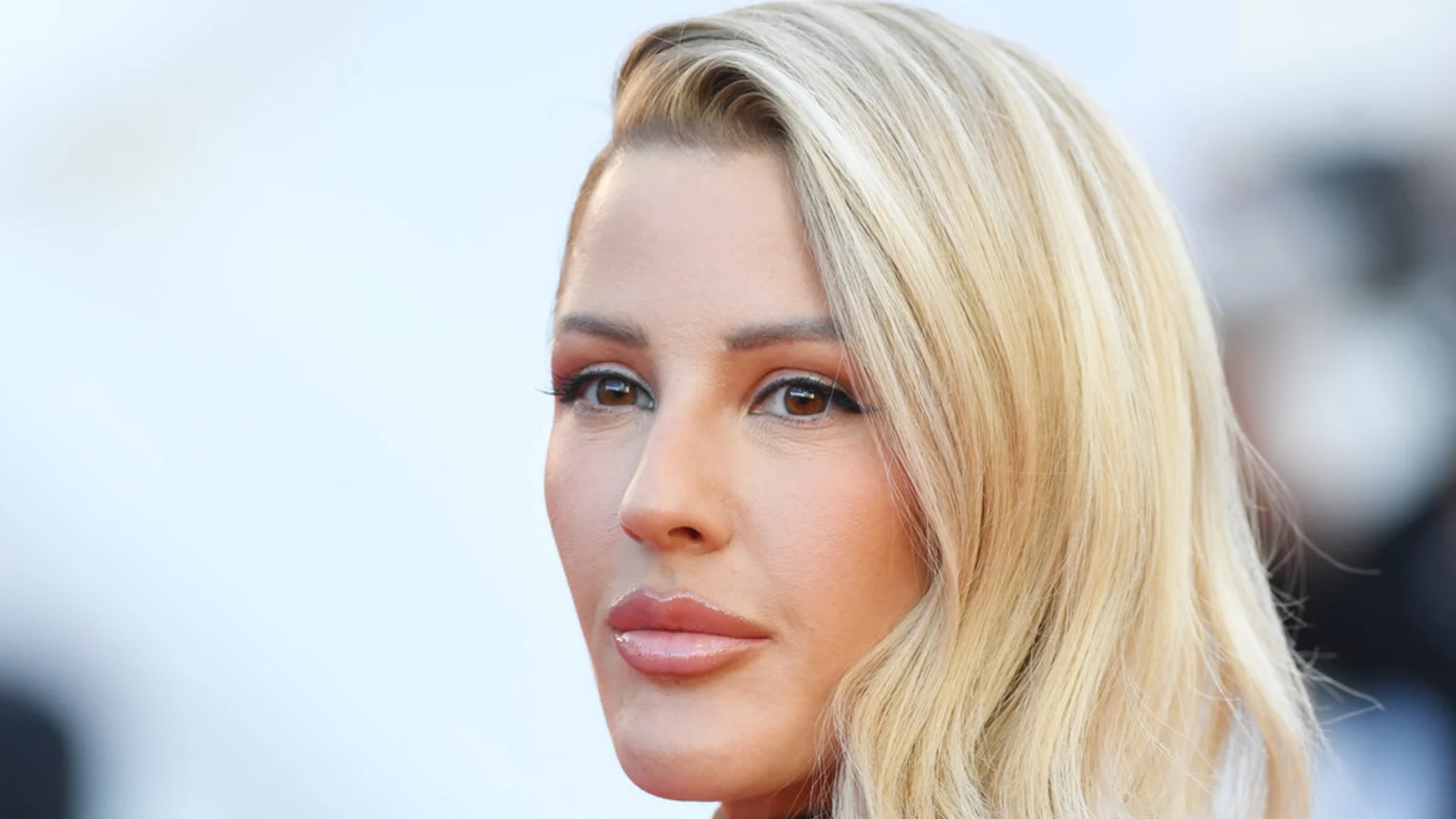 Close-up side profile of a woman with blonde hair, brown eyes, and full, glossy lips, looking to the right.