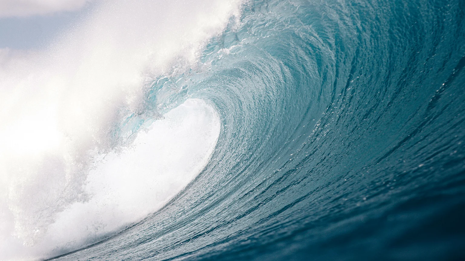 A large, powerful ocean wave with a curling barrel of deep turquoise water breaks with white foam and spray across its crest.