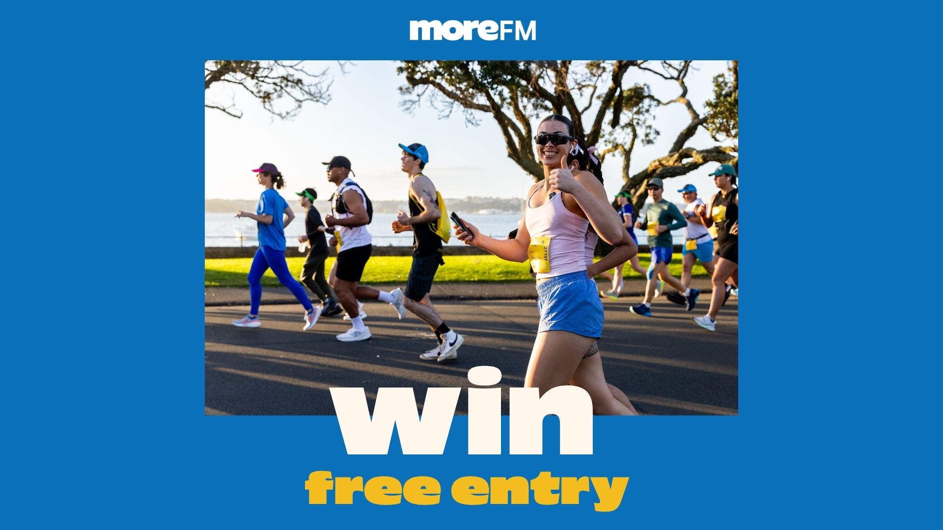 A smiling woman in a race bib gives a thumbs-up while running with other participants outdoors, with a "moreFM" logo and "Win free entry" text.