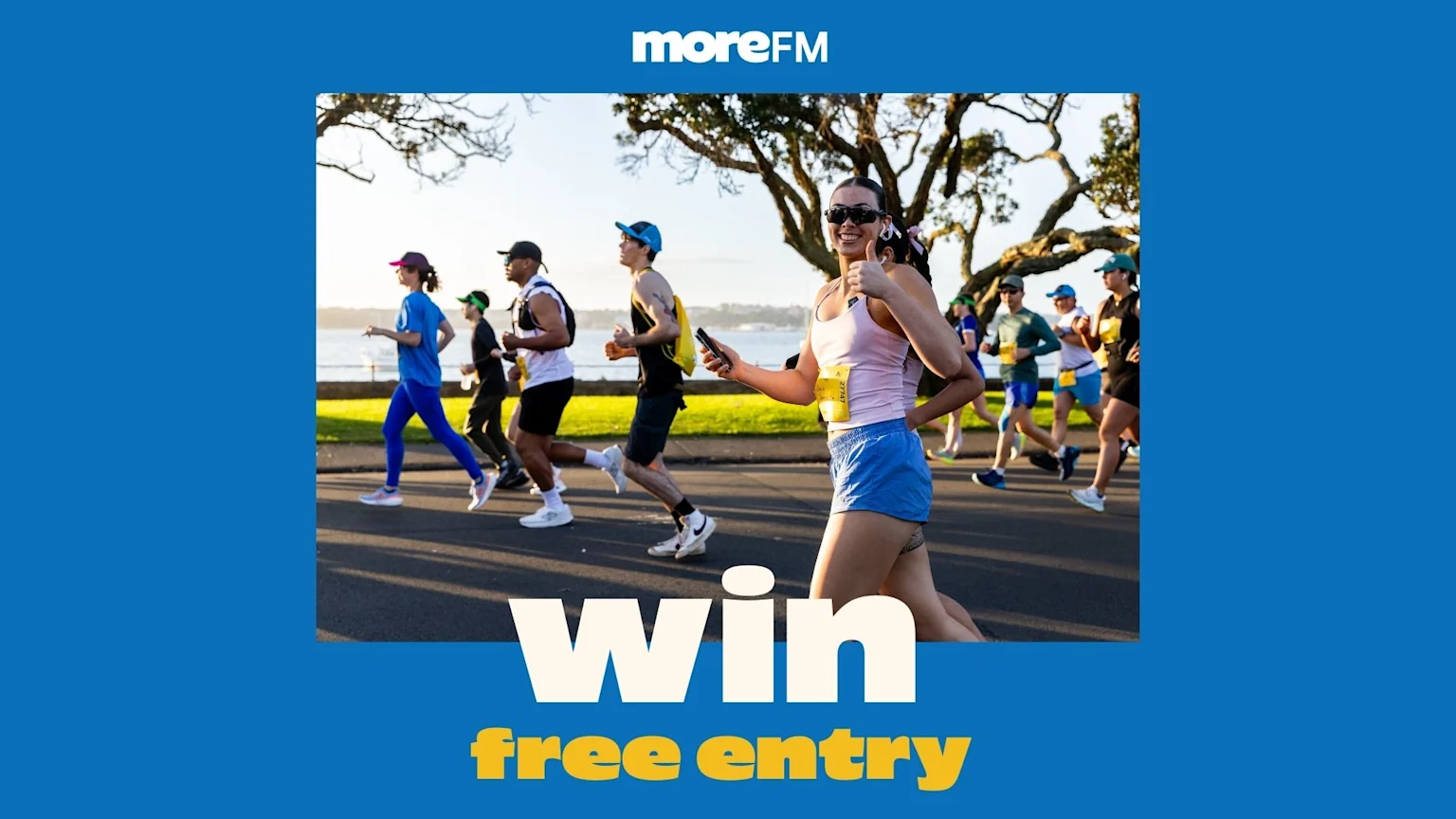 A smiling woman in a race bib gives a thumbs-up while running with other participants outdoors, with a "moreFM" logo and "Win free entry" text.