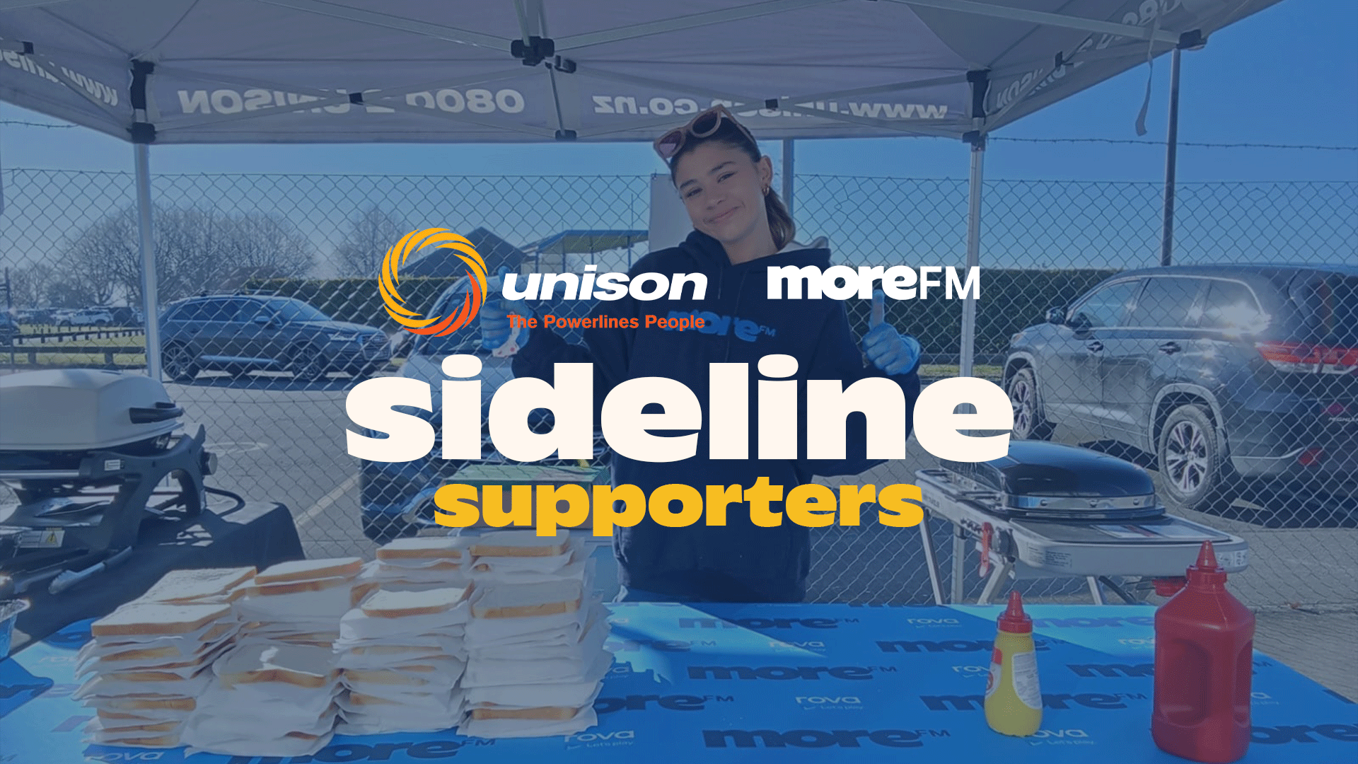A young woman gives a thumbs up behind a table with stacks of wrapped sandwiches, a grill, and condiment bottles, with Unison and More FM logos and "sideline supporters" text overlaying the scene.