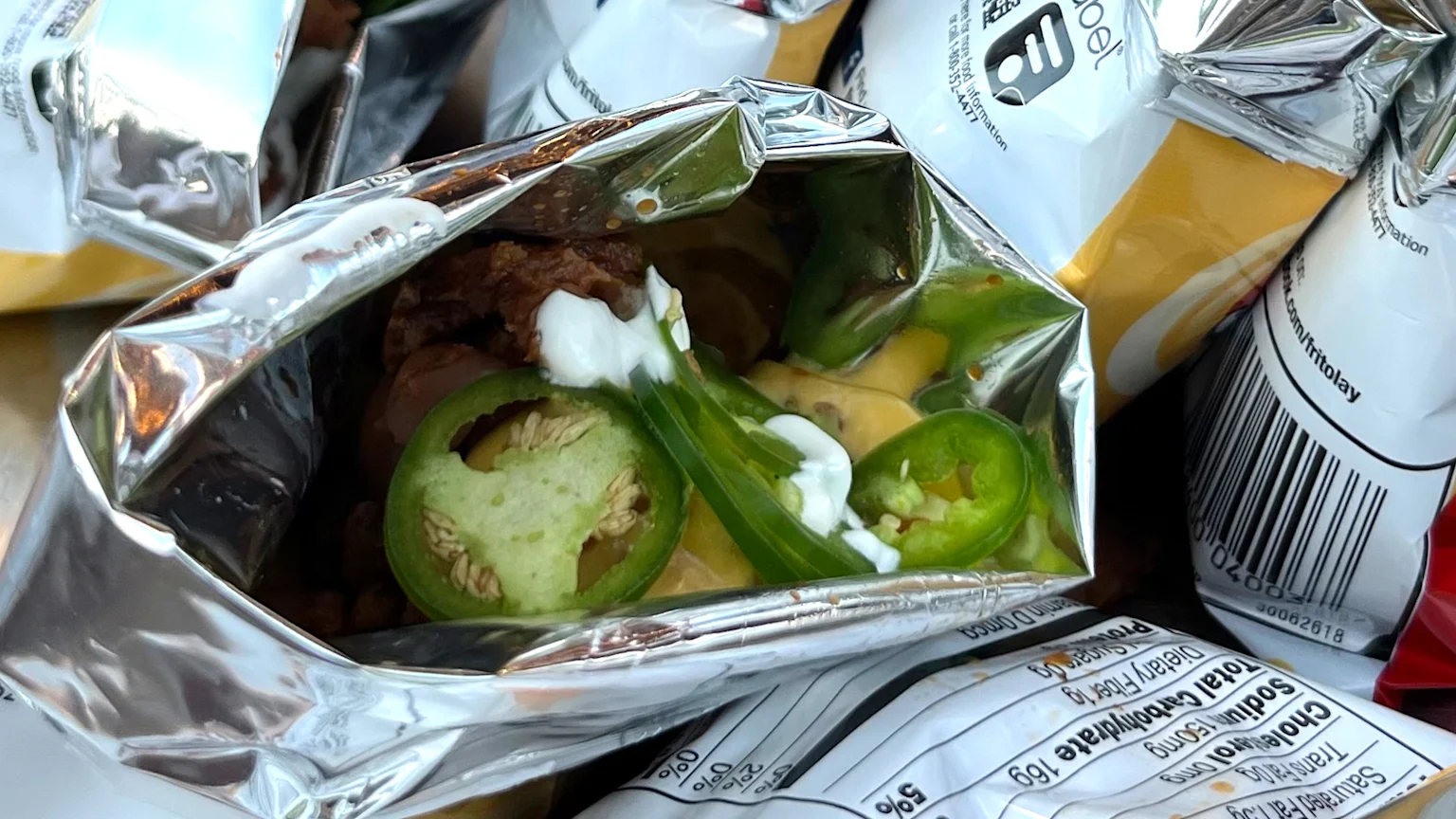 A bag of Frito's corn chips filled with a nacho mix and bright green jalapeno peppers.