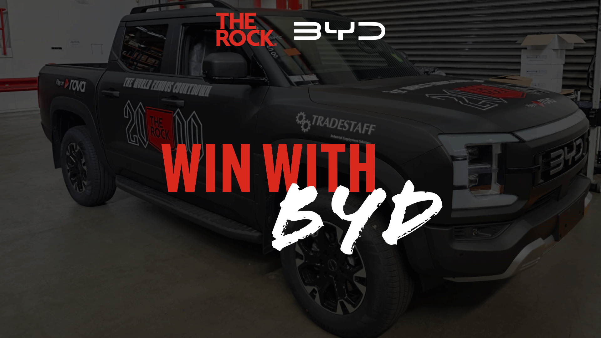 A black BYD pickup truck with "THE ROCK" logo on its side and hood, featuring overlaid text "WIN WITH BYD" in red and white.