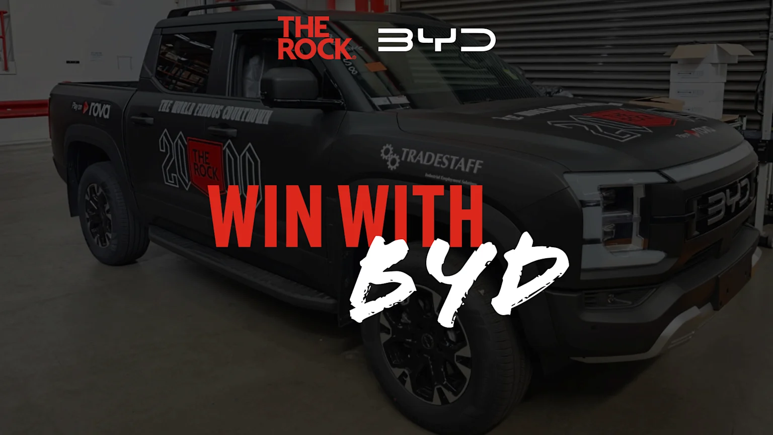 A black BYD pickup truck with "THE ROCK" logo on its side and hood, featuring overlaid text "WIN WITH BYD" in red and white.