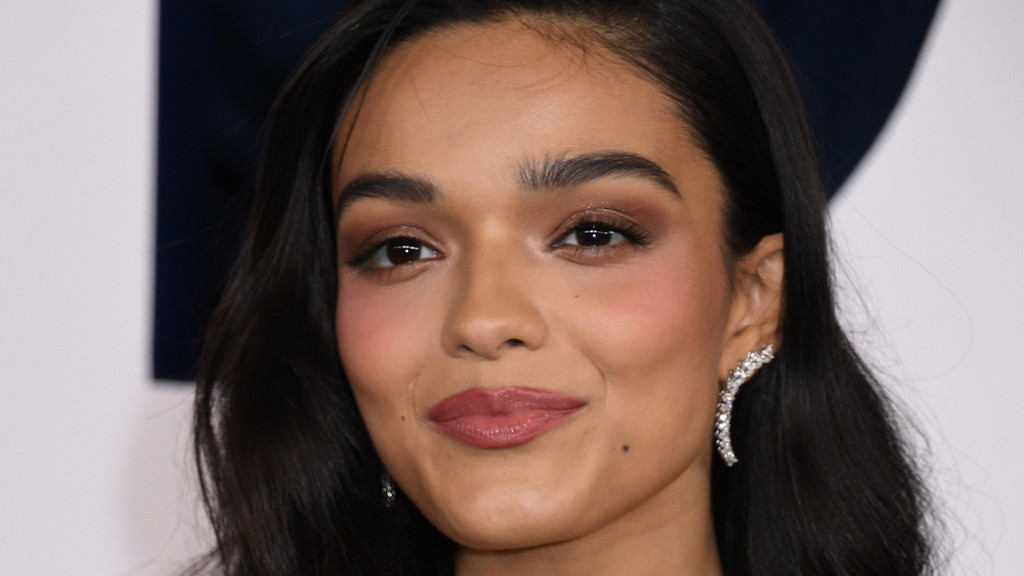 Close-up of Rachel Zegler smiling, with dark hair, brown eyes, defined eyebrows, subtle makeup, and a sparkling climber earring.
