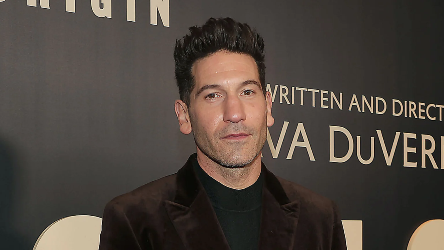 Jon Bernthal looks at the camera, wearing a brown velvet blazer and black turtleneck, against a dark background with text including "WRITTEN AND DIRECTED BY AVA DUVERNAY".