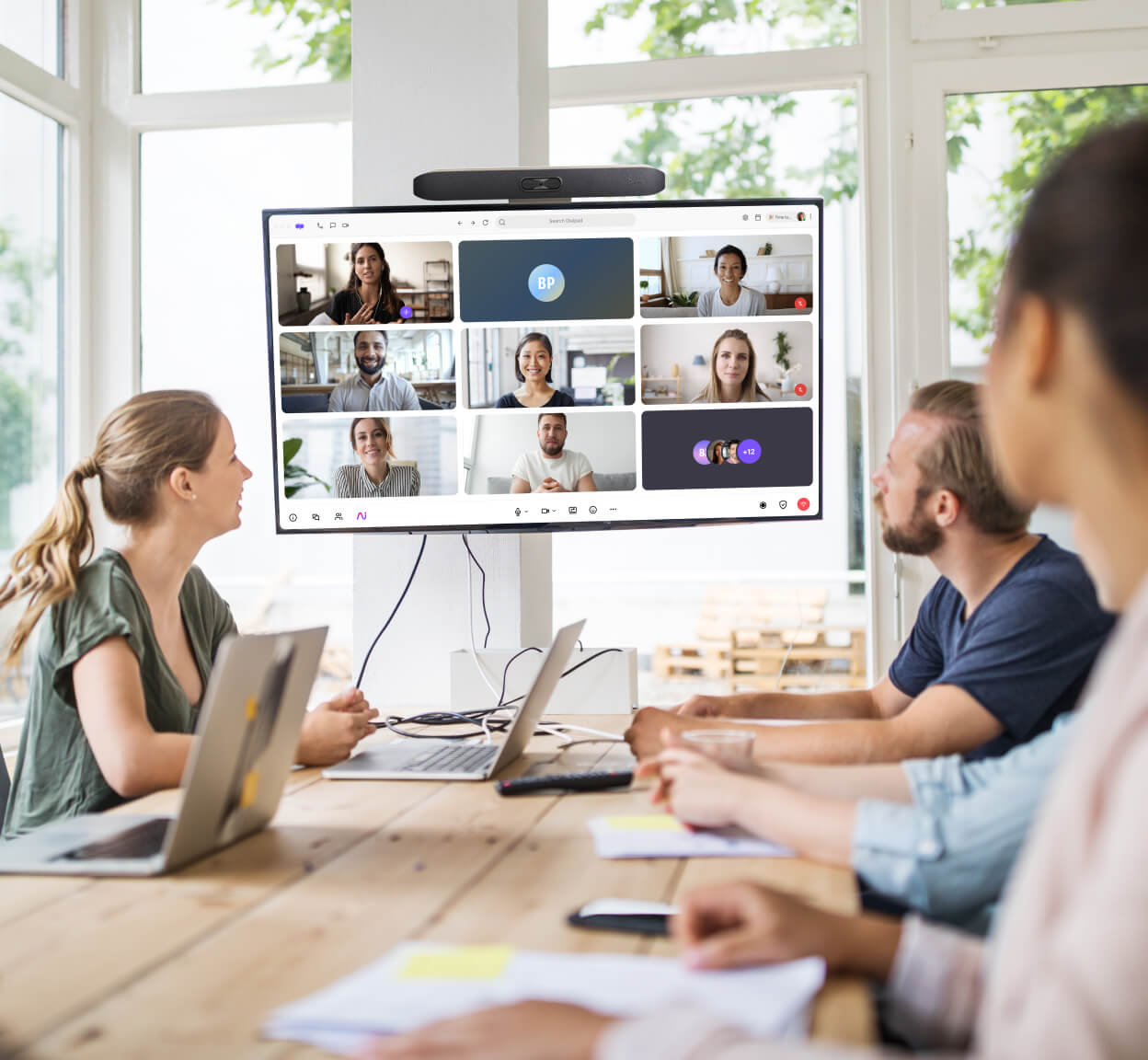 A group of people in a modern office participating in a Dialpad video conference displayed on a large screen