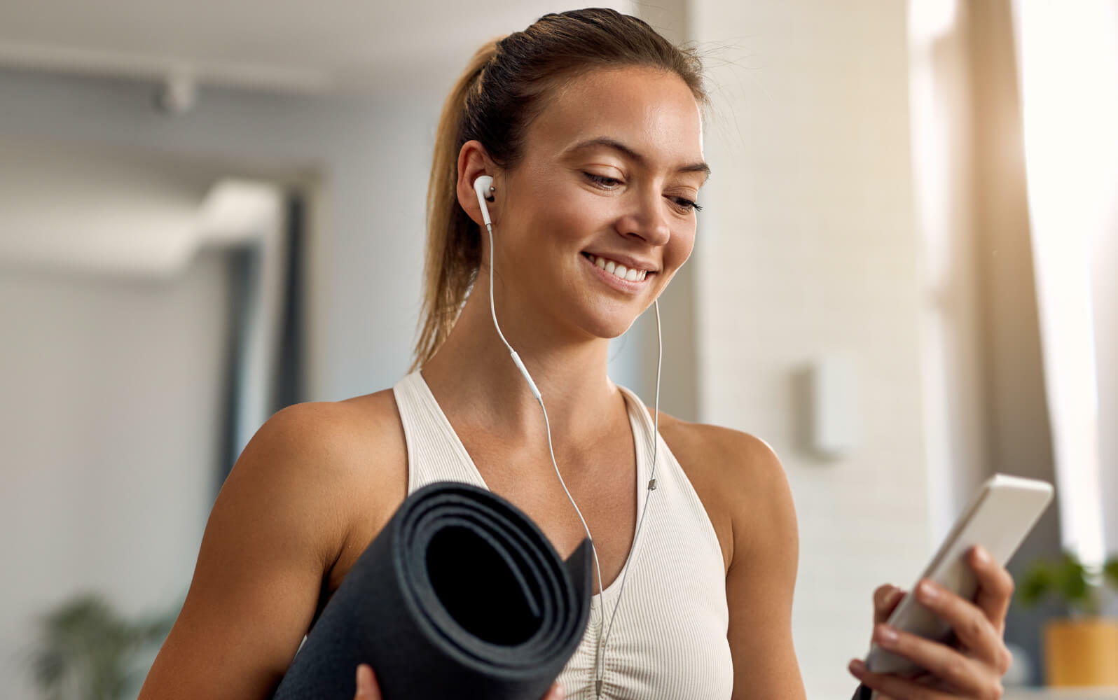 A woman holding a mobile and yoga mat