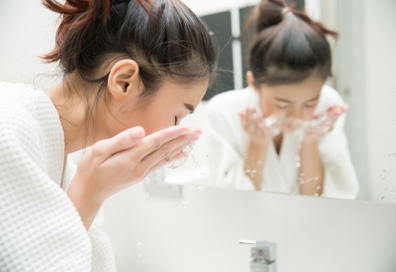 woman-washing-face-in-bathroom-mirror