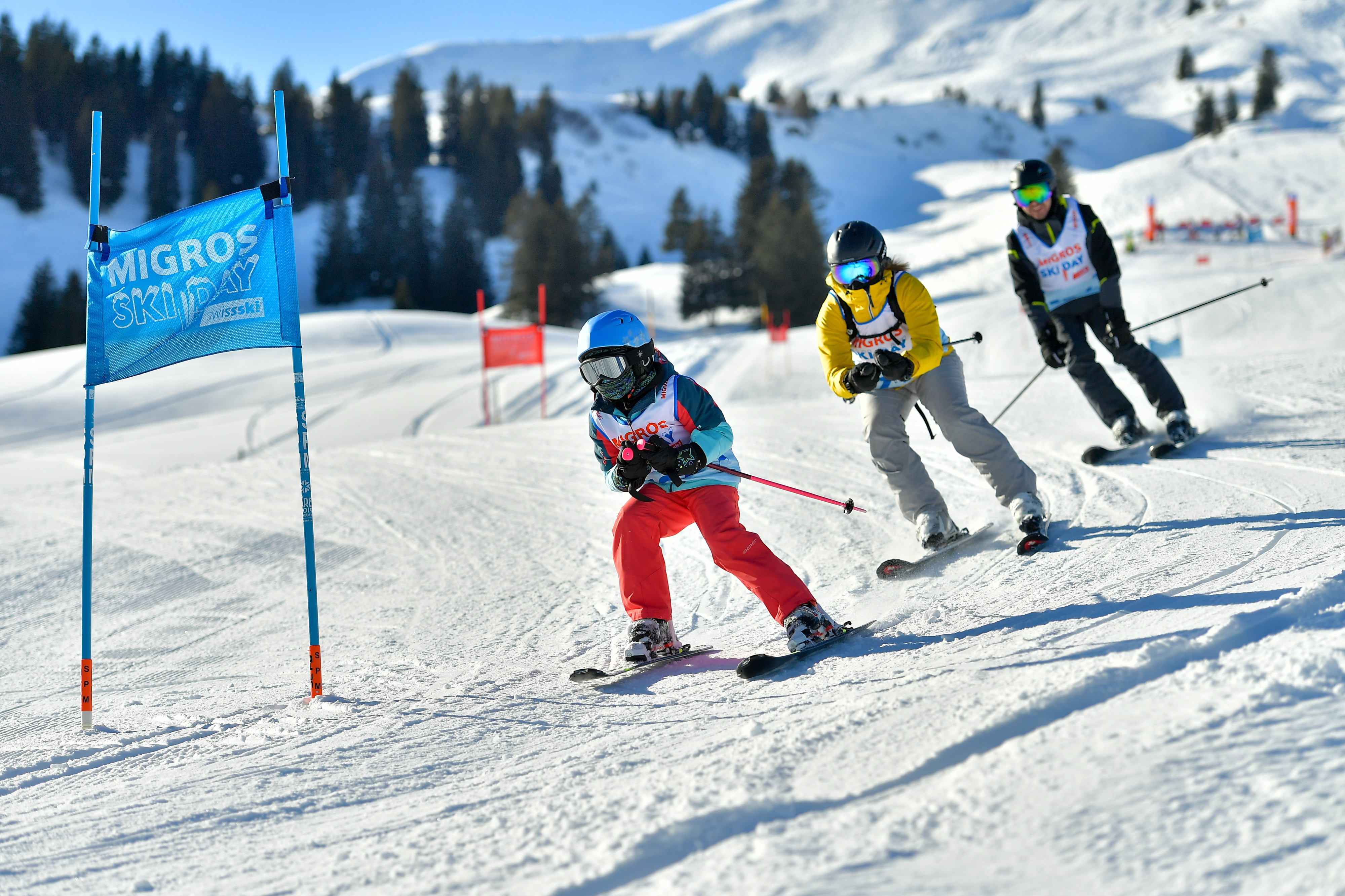 Drei Personen fahren mit Ski hintereinander Slalom einen Hang hinab.