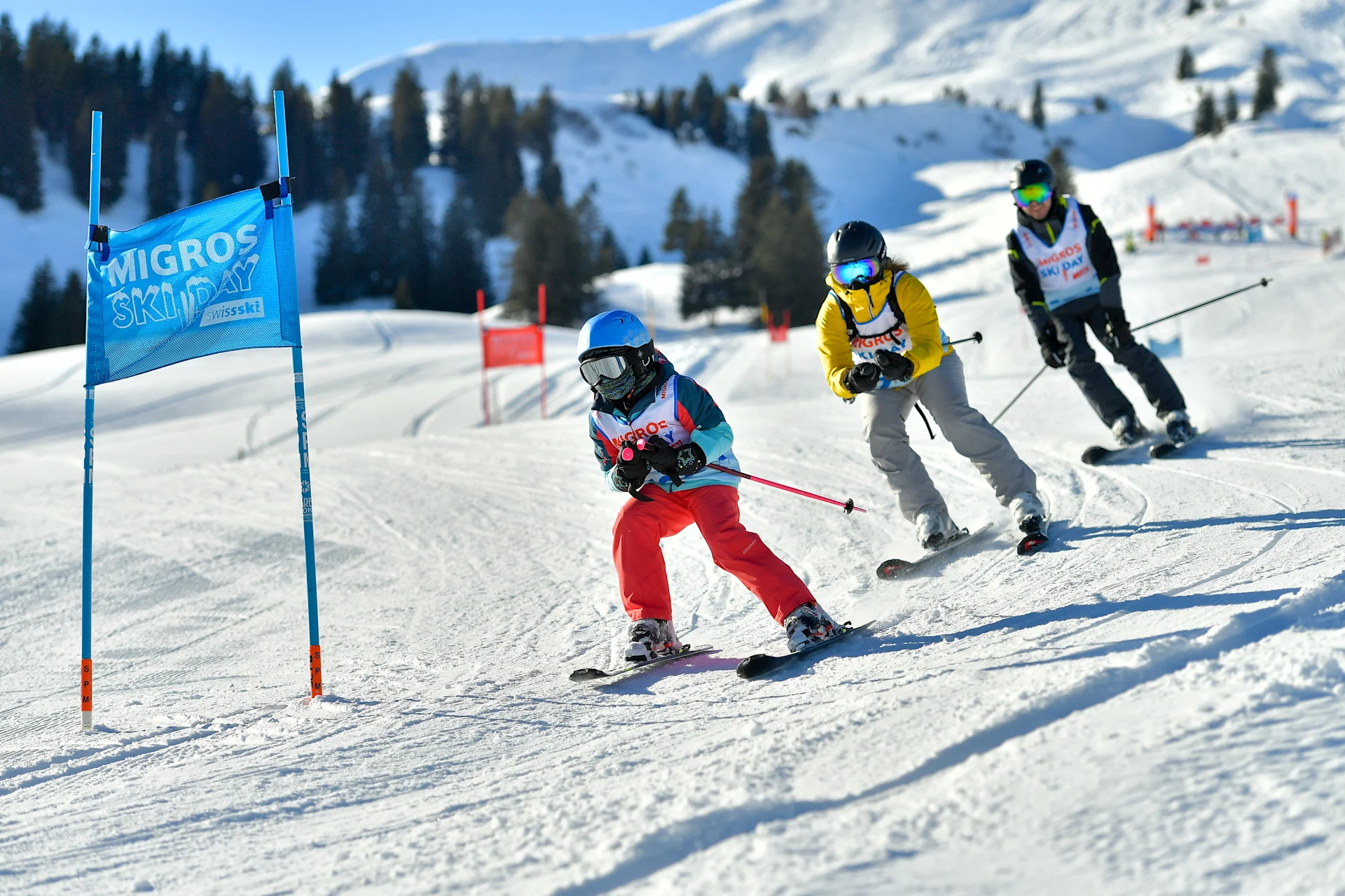 Three people ski slalom down a slope one after the other.