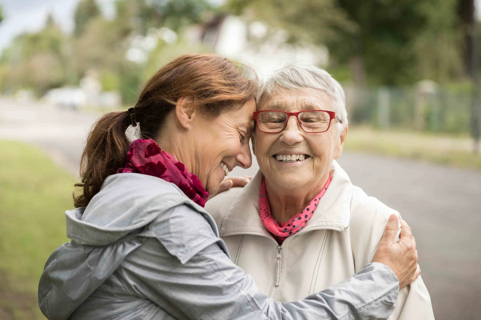 Eine lächelnde Frau umarmt eine ältere Frau, die ebenfalls lächelt.