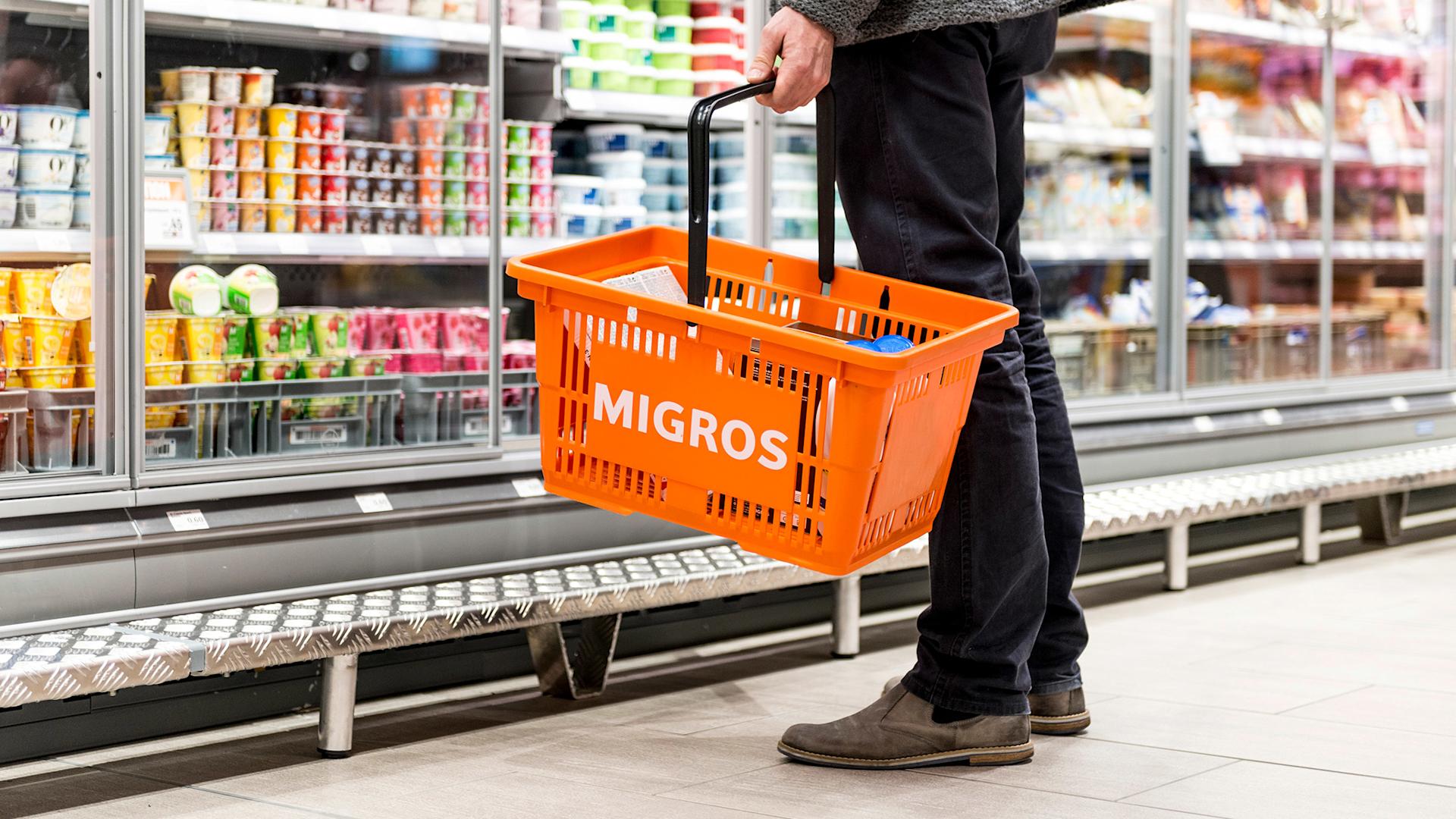 Un uomo con un cestino della spesa Migros davanti a un banco frigo in una filiale