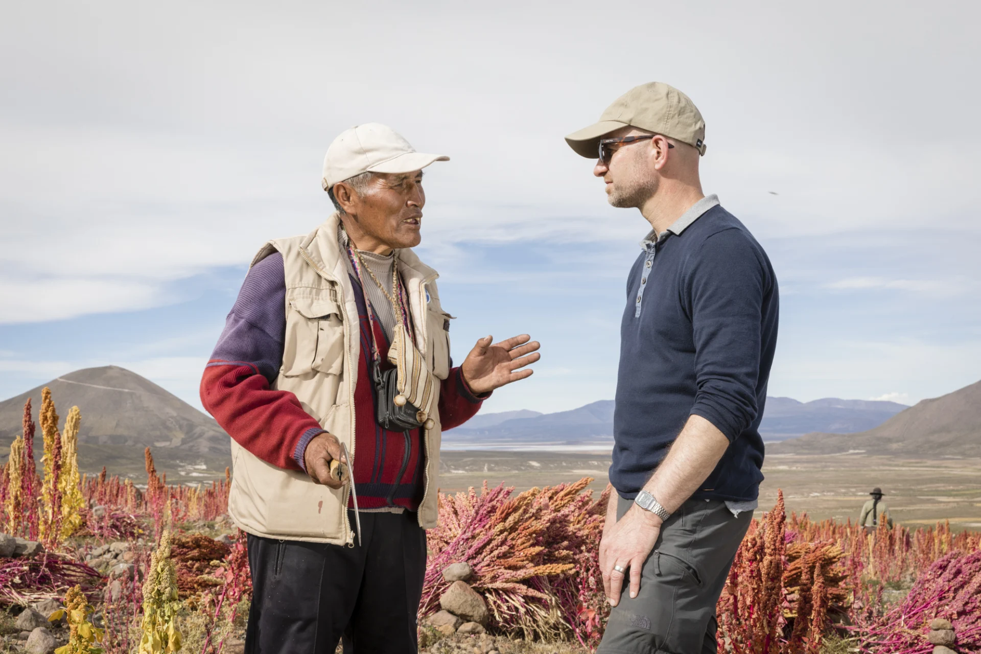 Two men talk in front of a quinoa field.