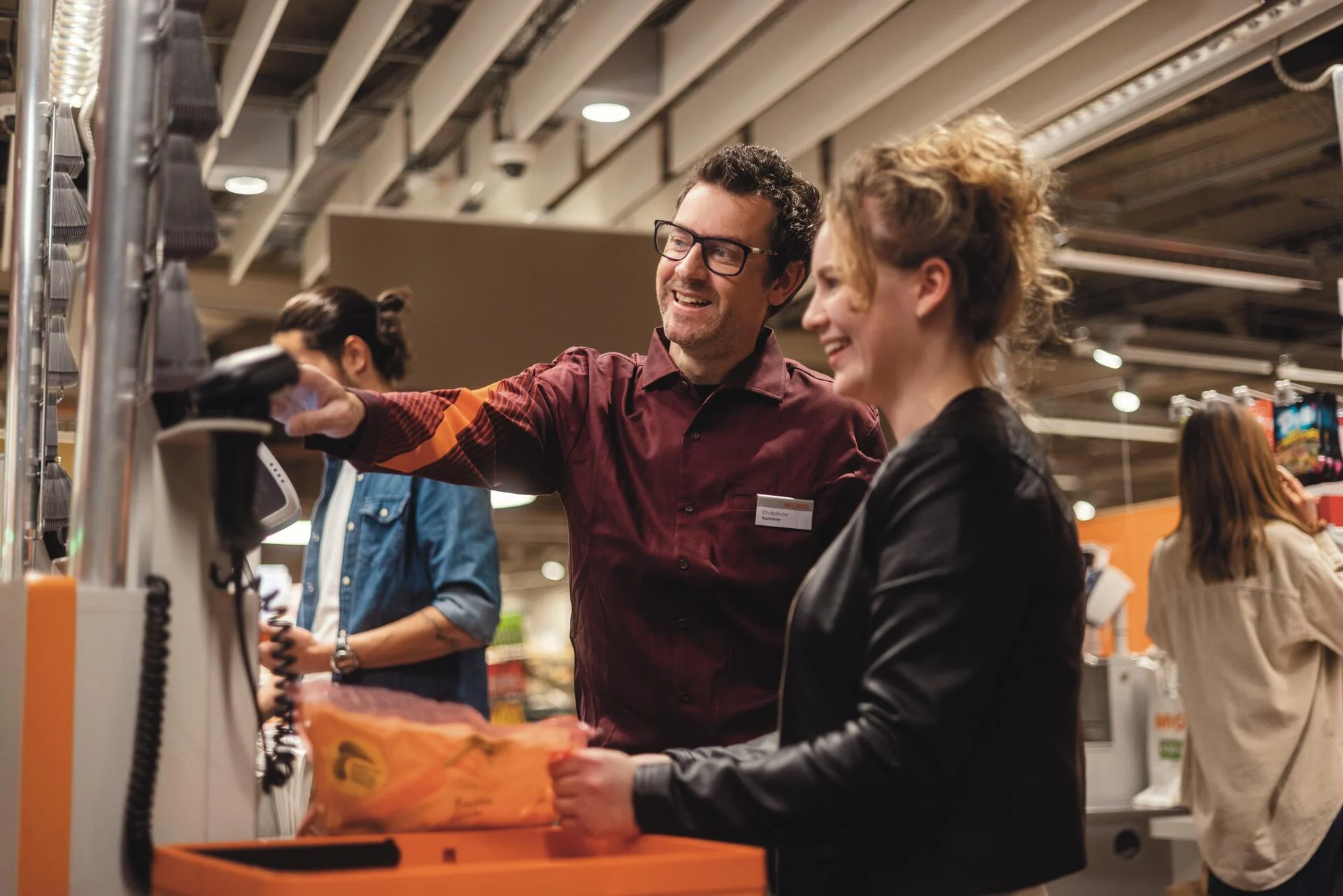 Ein Mitarbeiter in einer Migros-Filiale hilft einer Kundin an einer Self-Scanning-Kasse.