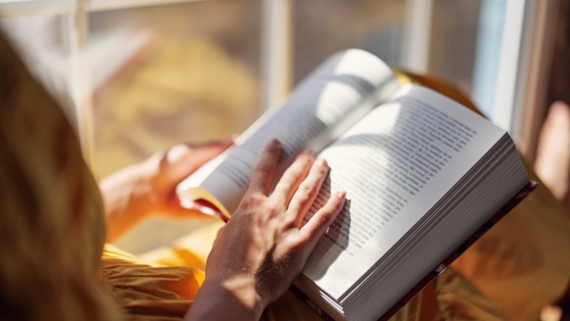 Jugendliches Mädchen liest ein Buch auf einer Fensterbank in der Sonne