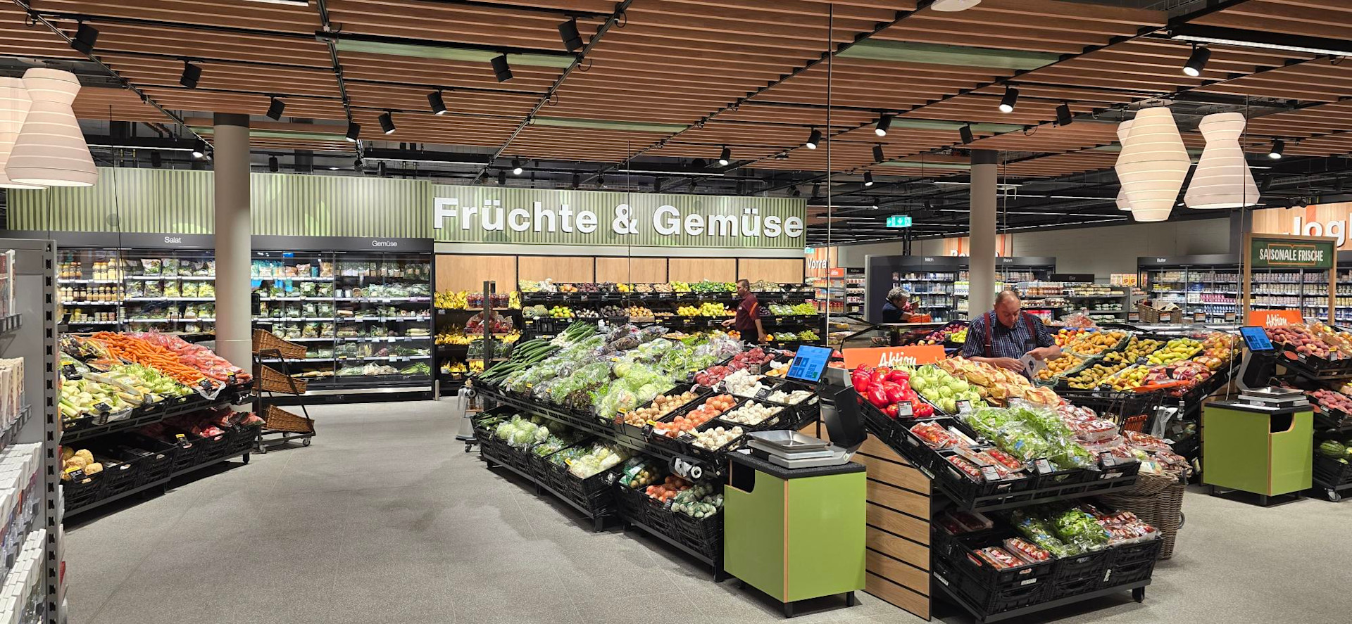Frischeabteilung eines modernen Migros-Supermarkts mit grosszügiger Präsentation von Gemüse und Früchten, gut ausgeleuchteten Regalen und übersichtlicher Warenanordnung.