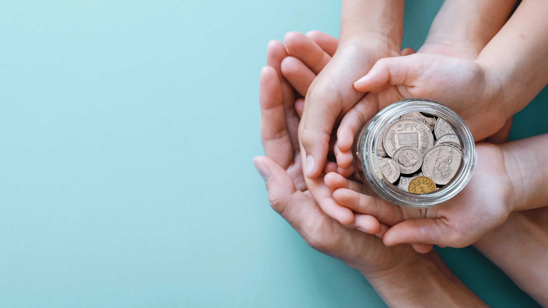 Three pairs of hands clasp a glass with coins