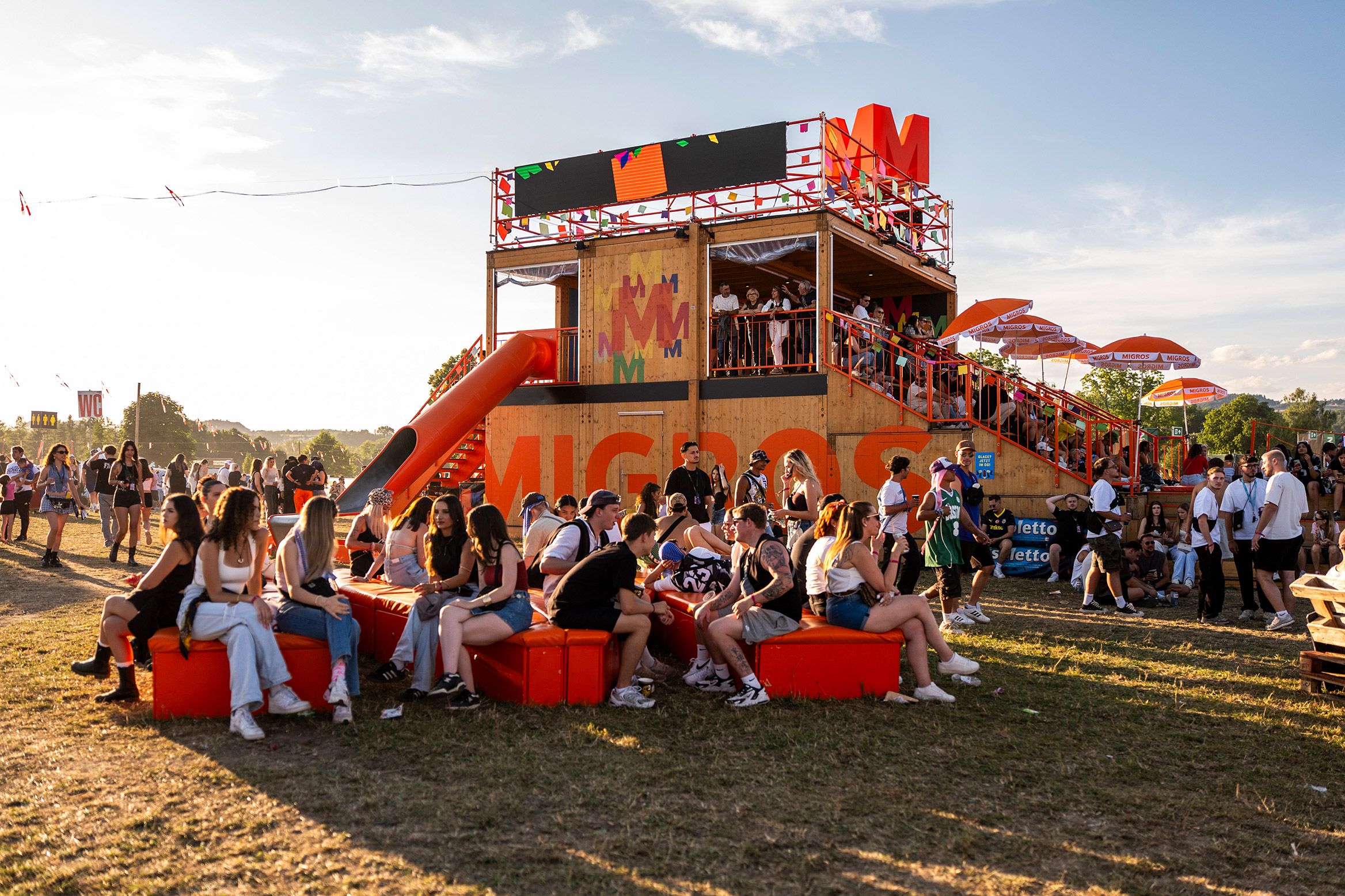 Young people are sitting at the Migros stand on the festival grounds.