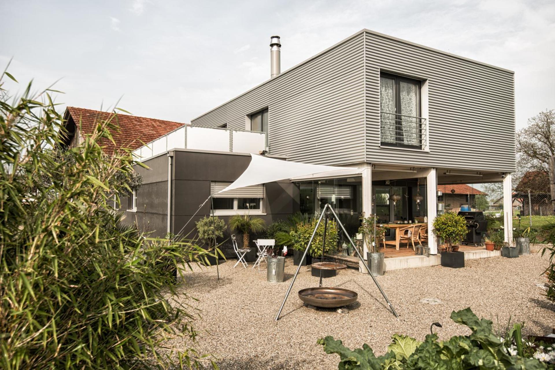 Une maison individuelle moderne avec terrasse, des plantes pour la végétation et un gril.