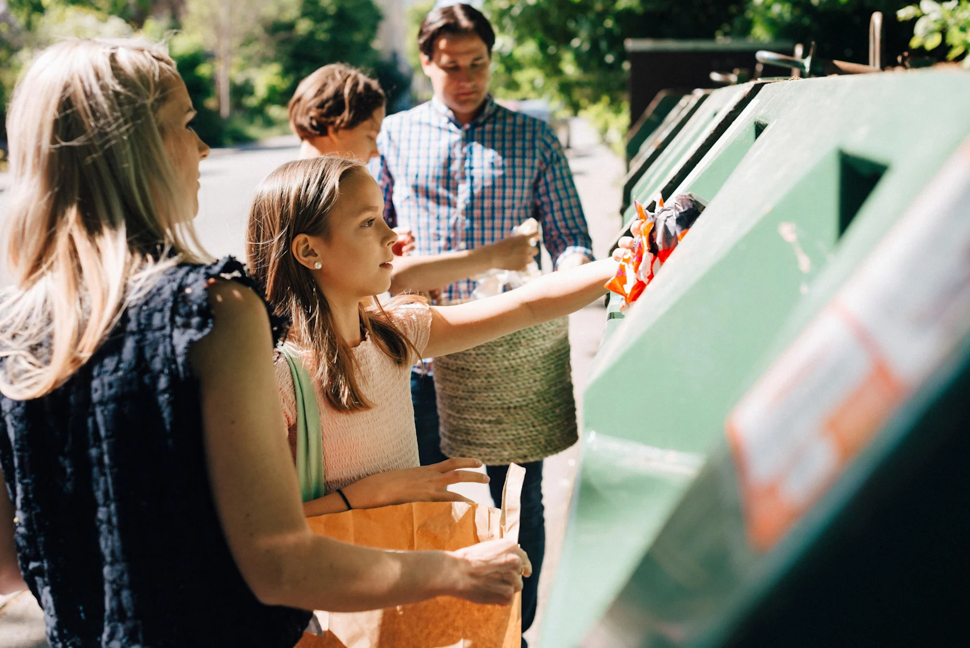 Une famille se tient devant un point de collecte et la fillette y jette des déchets plastiques.