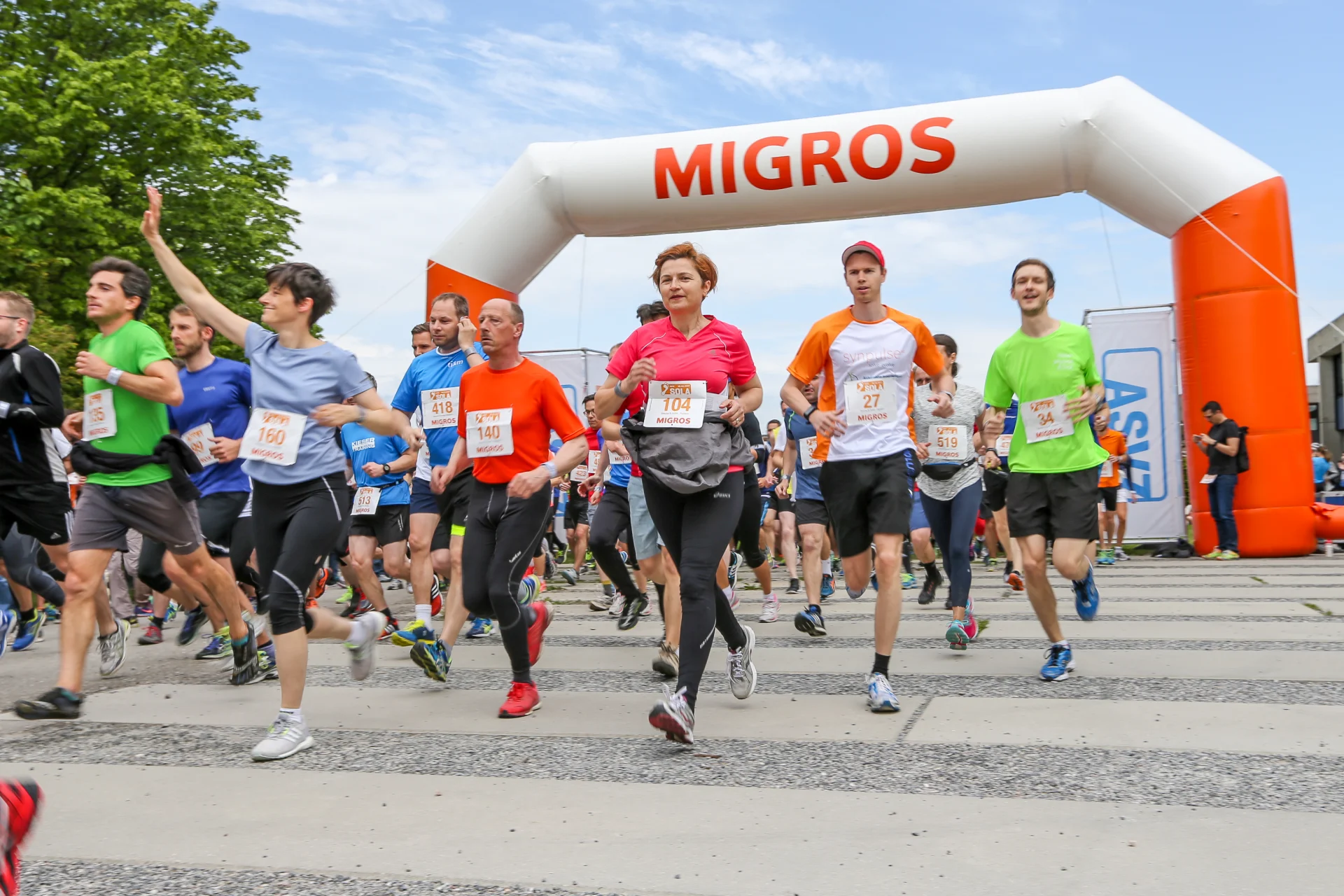 Runners passing under an inflatable Migros archway.
