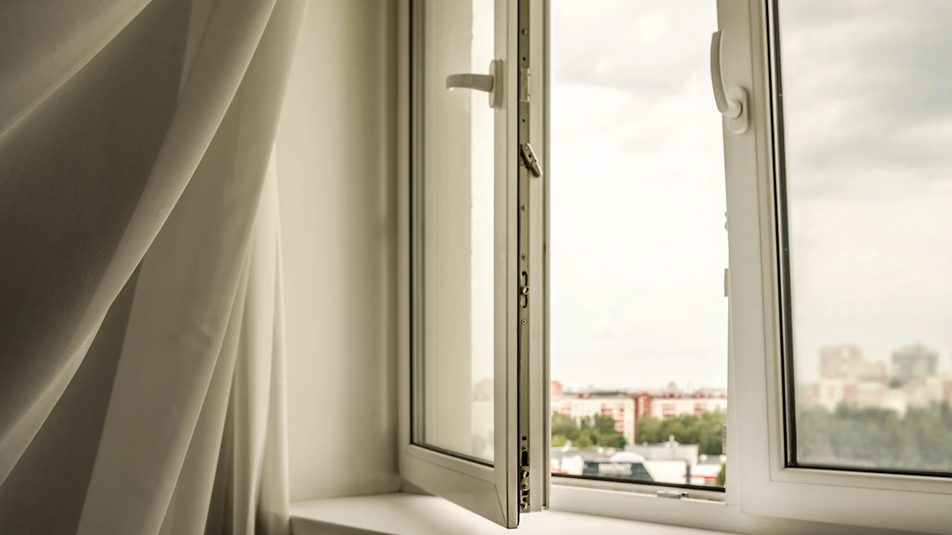 A curtain is blown open by the breeze in front of a wide-open window.