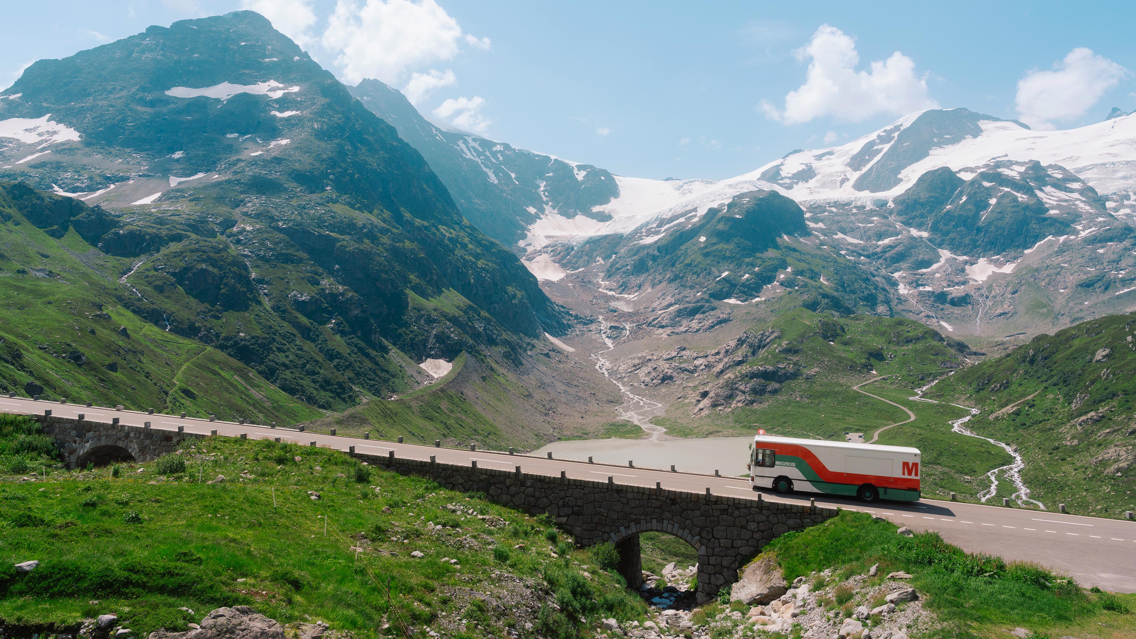 Le bus Migros roule le long d'une route de montagne.