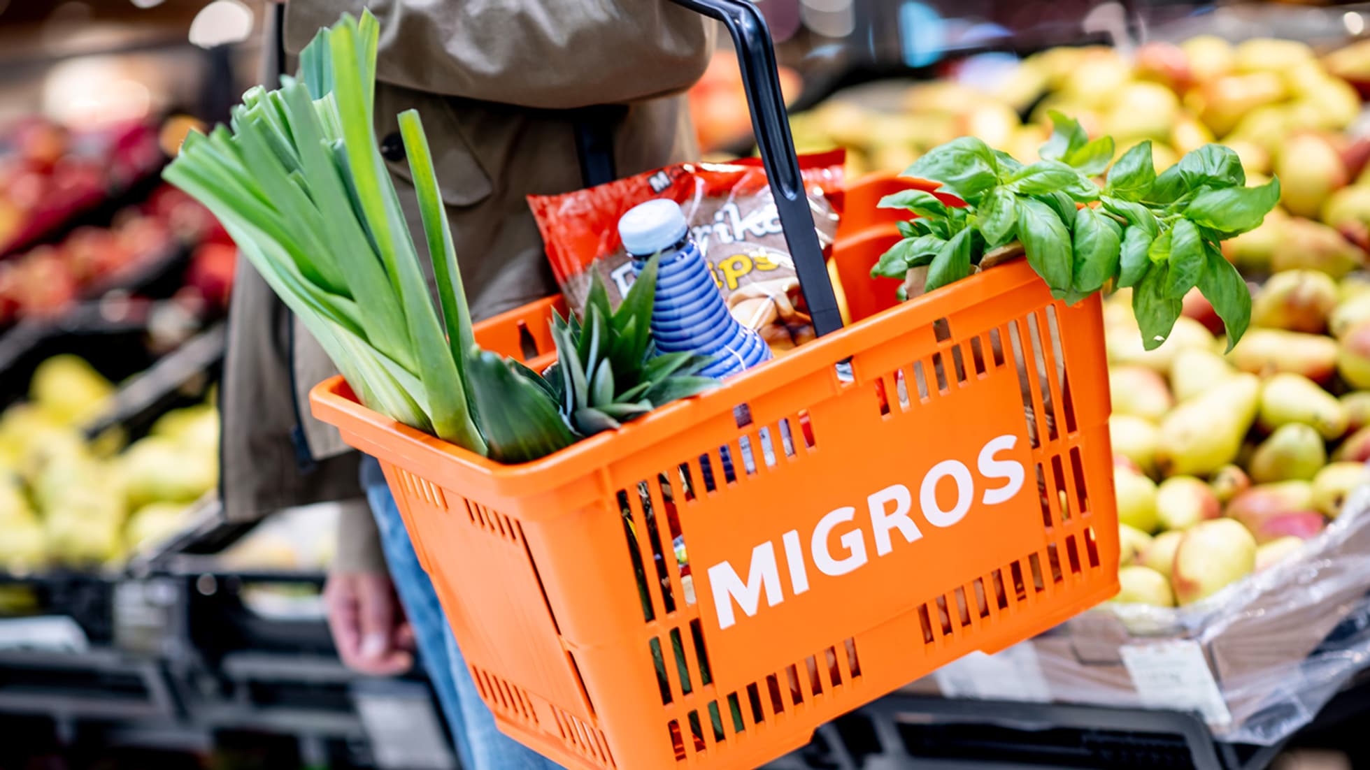 Ein oranger Migros-Einkaufskorb gefüllt mit Produkten.