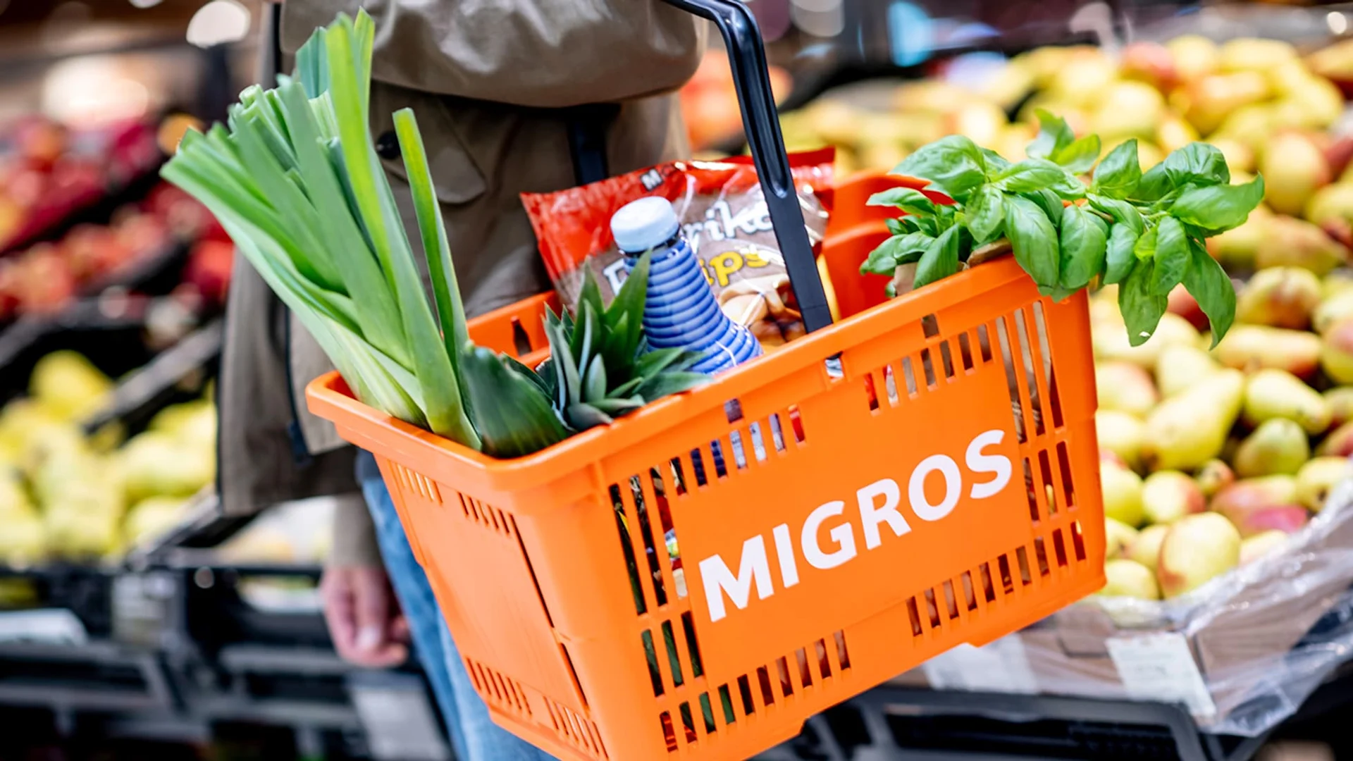 Ein oranger Migros-Einkaufskorb gefüllt mit Produkten.
