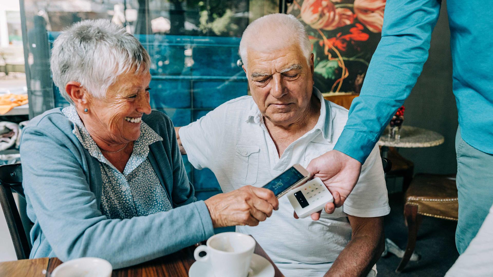 Eine ältere Frau zahlt im Restaurant kontaktlos mit ihrem Telefon.