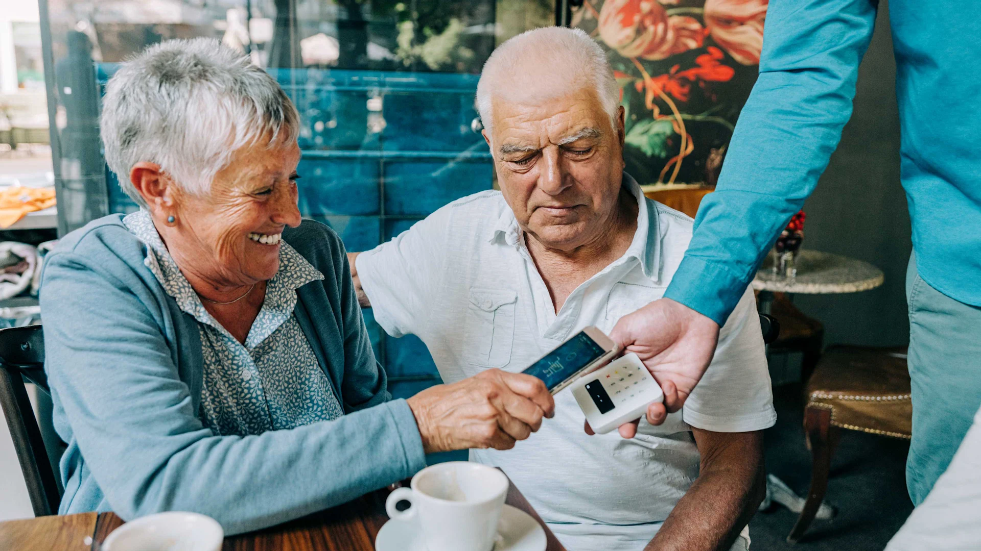 An elderly woman pays contactless with her phone in a restaurant.