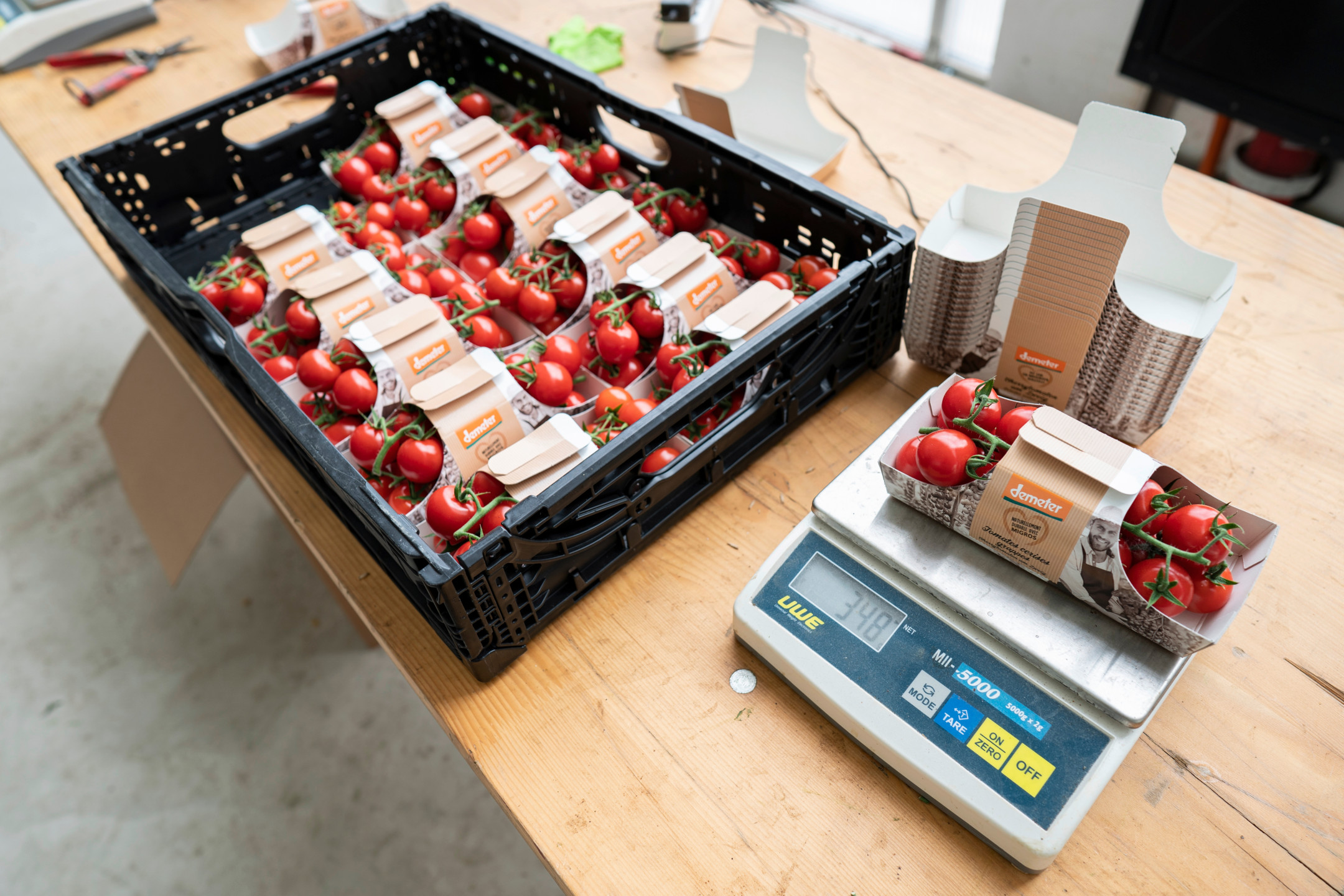 Une balance avec un paquet de tomates cerises sur le dessus, à côté d'une caisse de tomates cerises