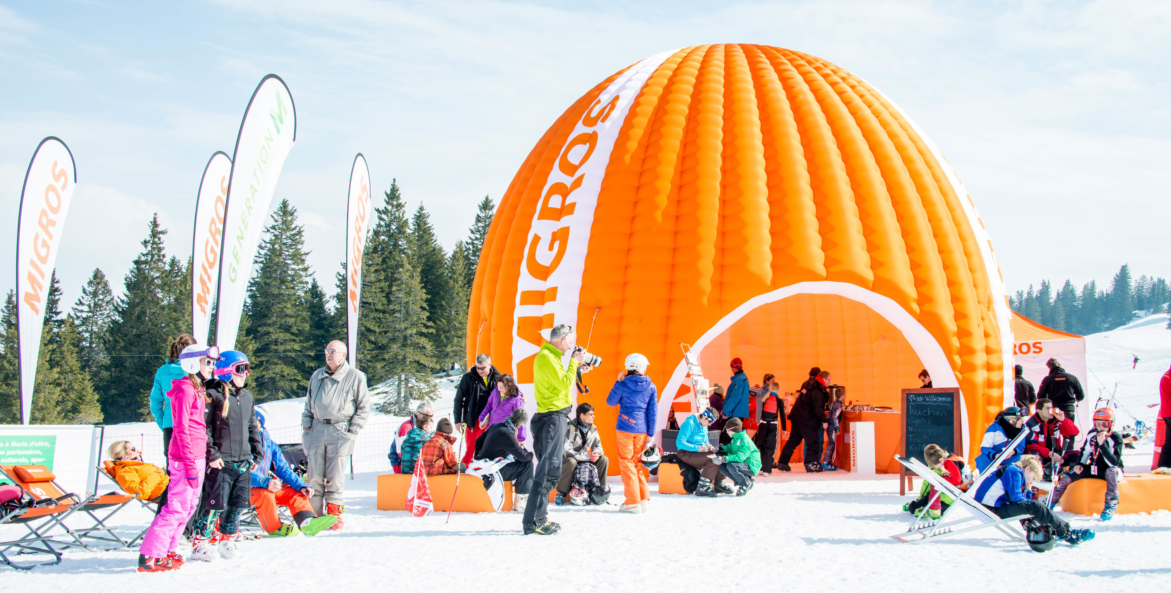A large orange Migros tent at a Grand Prix.