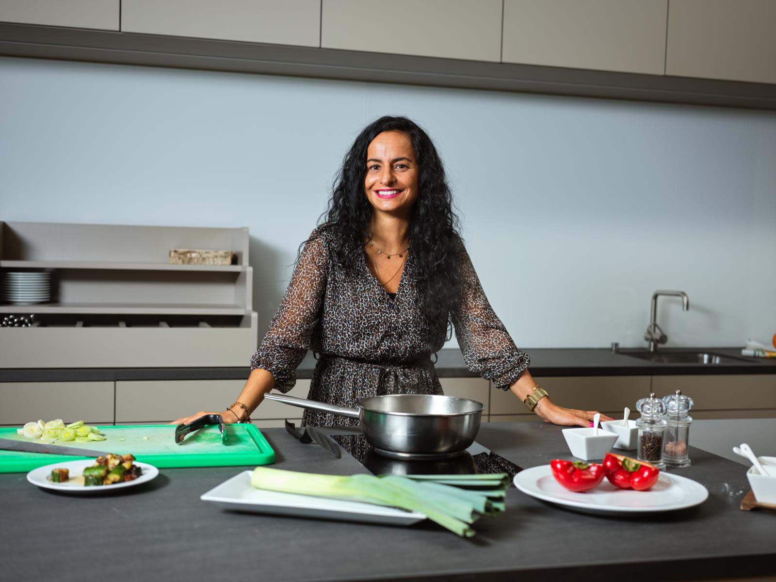 Nancy Da Silva stands in a kitchen, a pan and vegetables in front of her.