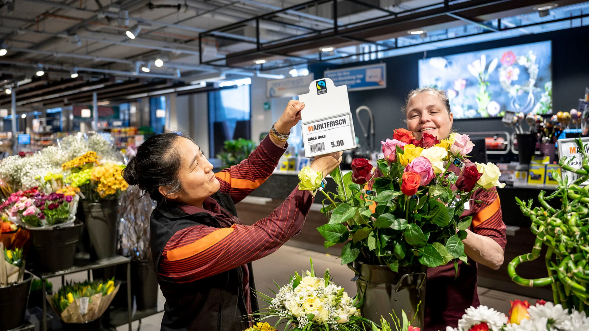 Deux collaboratrices de Migros installent un panneau affichant des roses Fairtrade.
