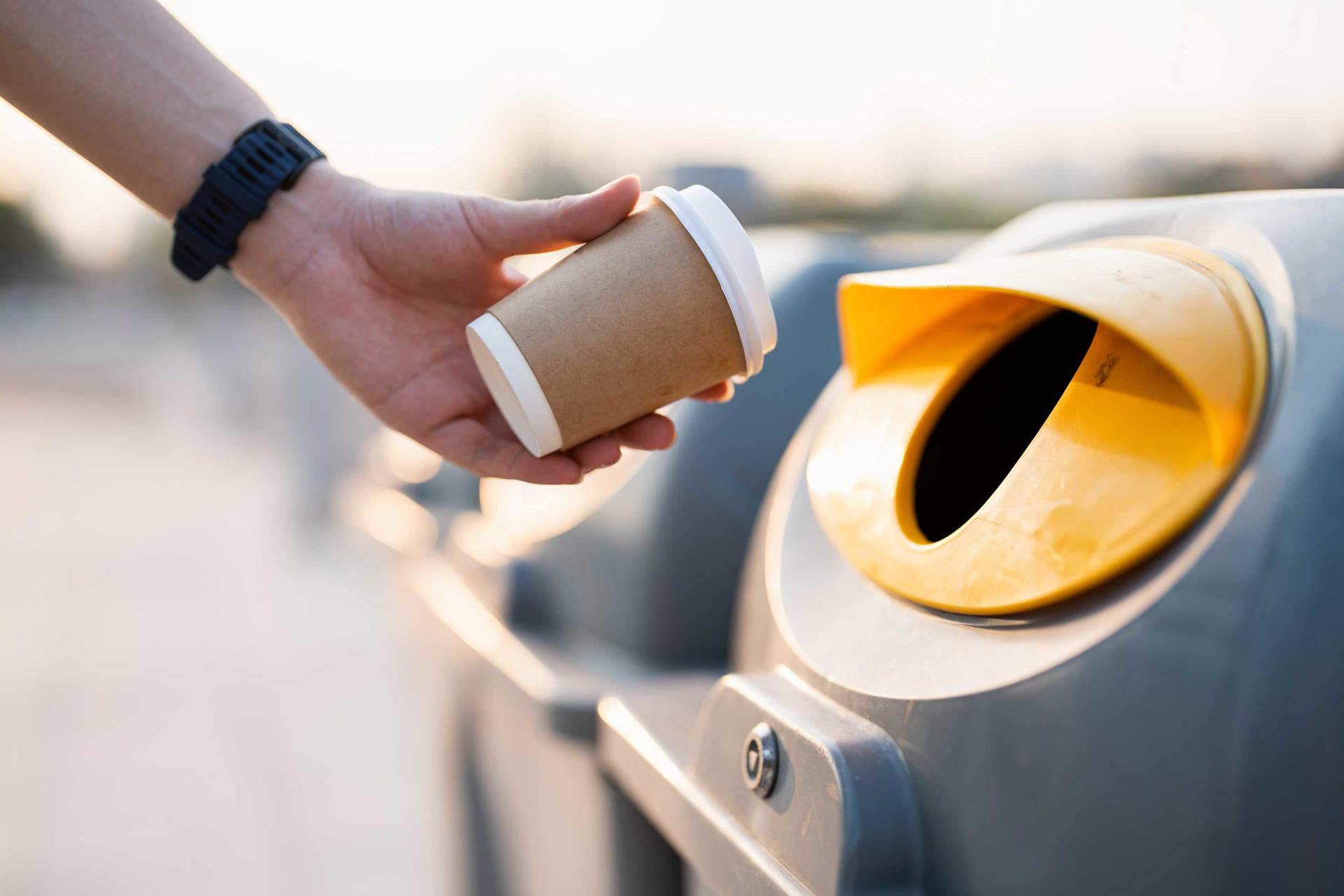 A person throws a paper cup into a litter garbage can