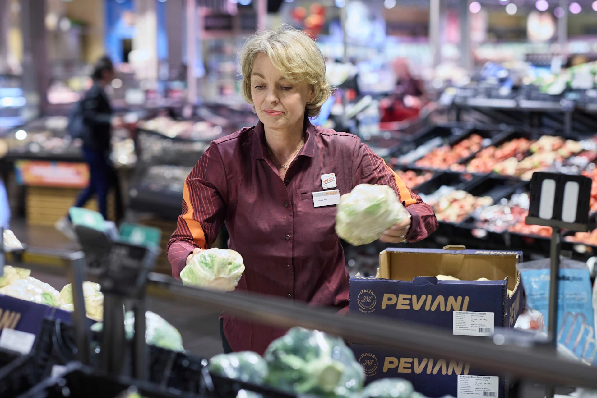 Ursula Nold, in einer orange-roten Migros-Bluse, räumt in der Gemüse-Abteilung Blumenkohl ein