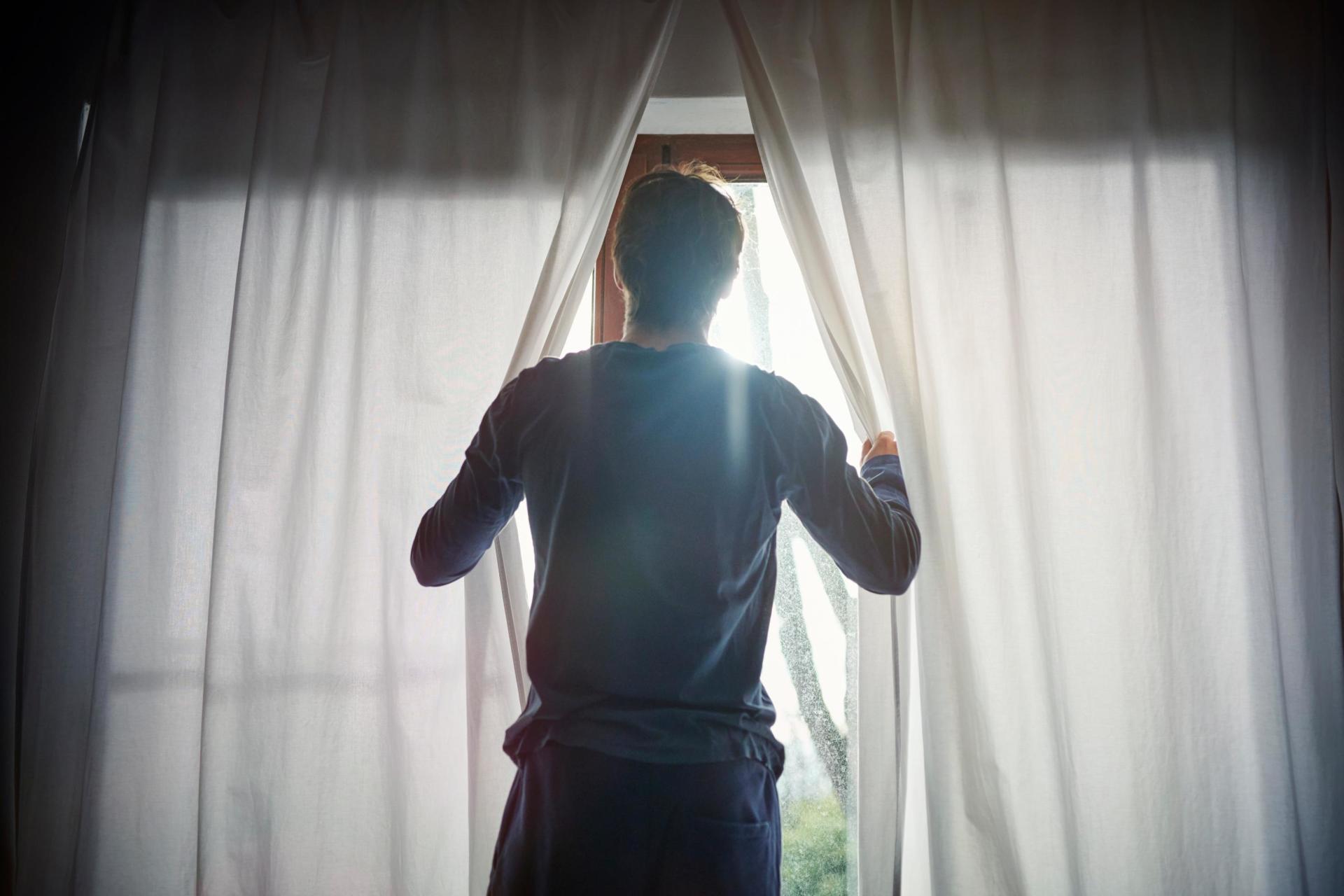A man opening the curtains to open the window.