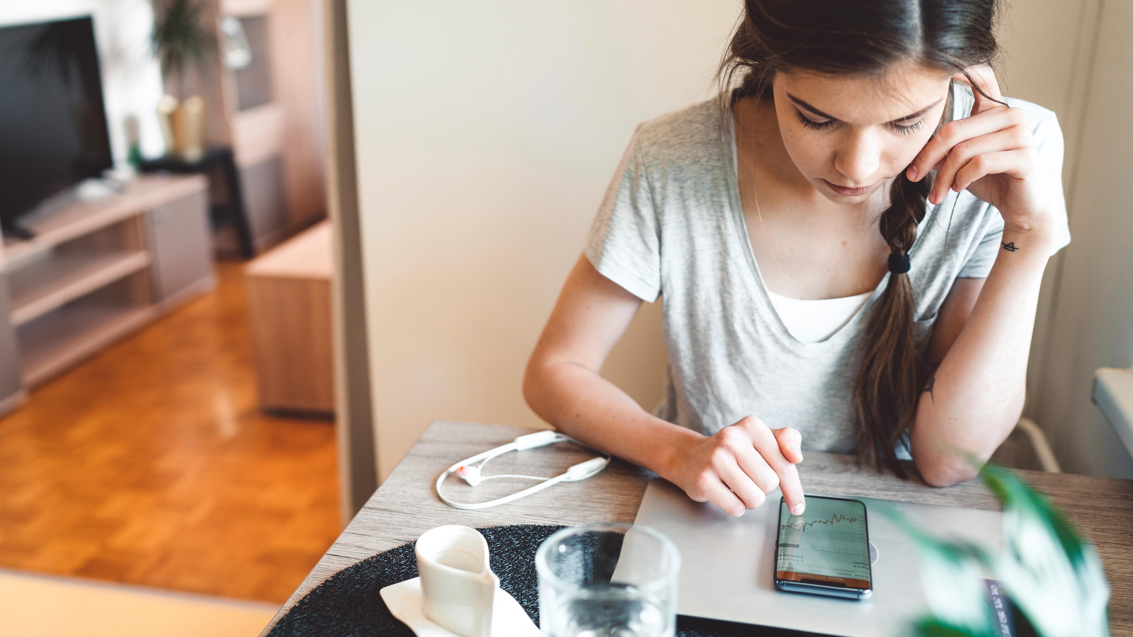 A young woman checks the performance of an investment on her smartphone.