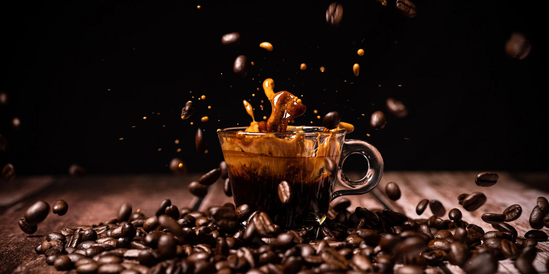 An espresso cup with espresso stands on coffee beans against a dark background.