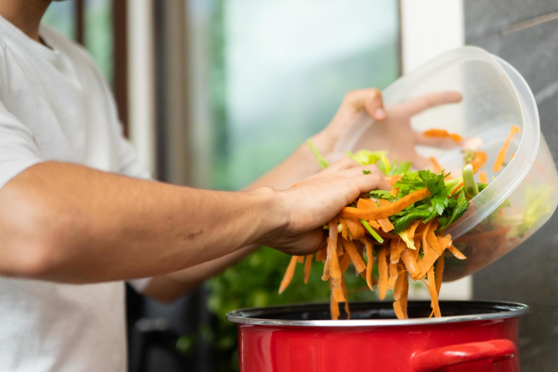 Un cuisinier verse des épluchures dans une casserole rouge