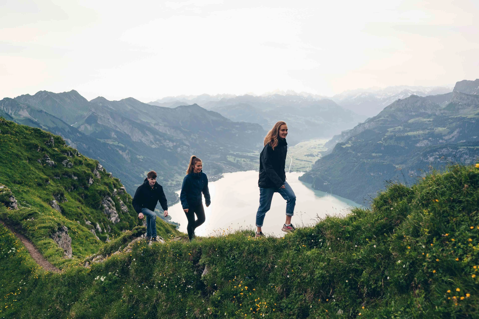 Three people hiking on a ridge, a mountain lake in the background.
