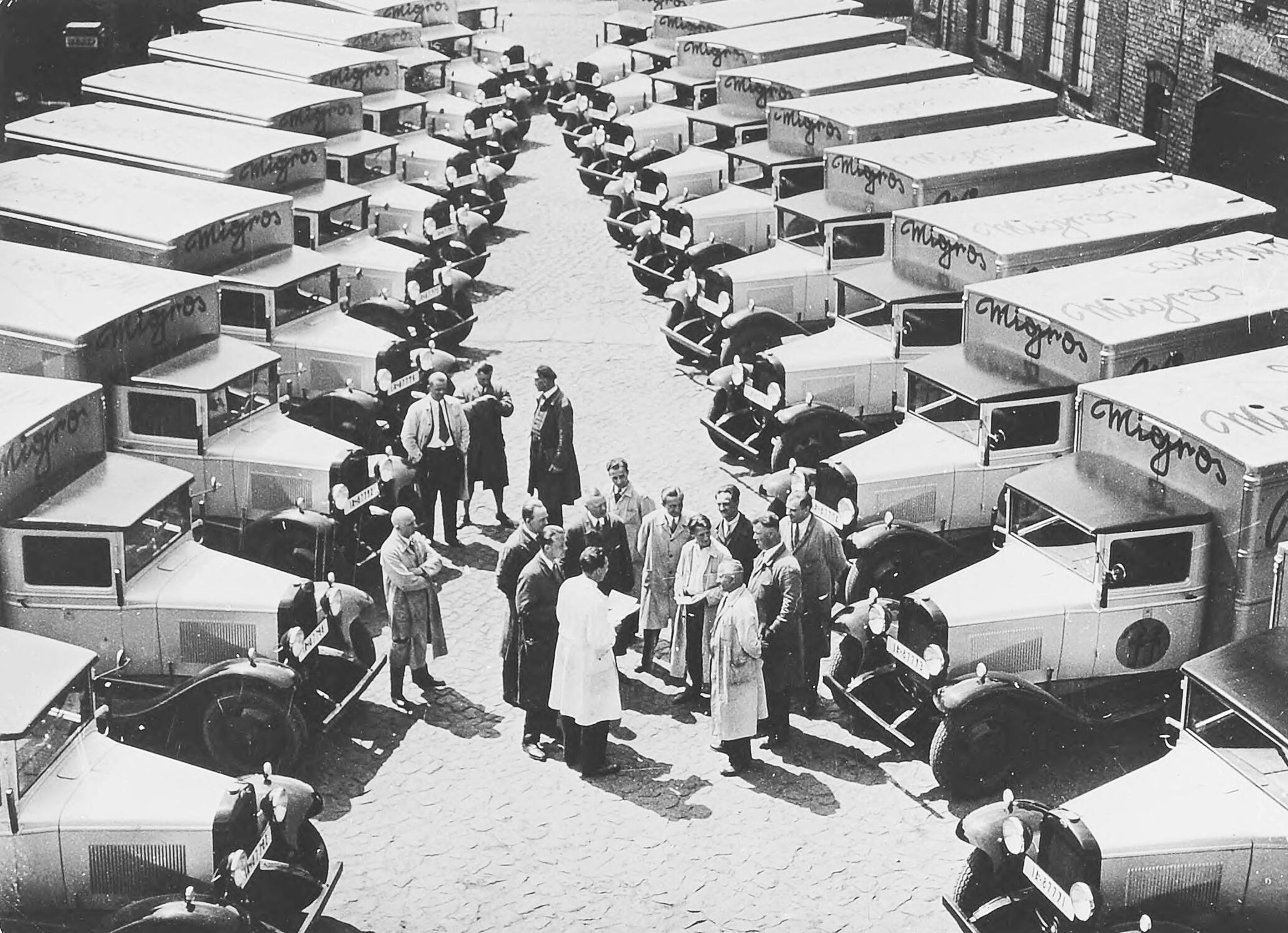 A black-and-white photograph of the Migros subsidiary's sales vans in Berlin