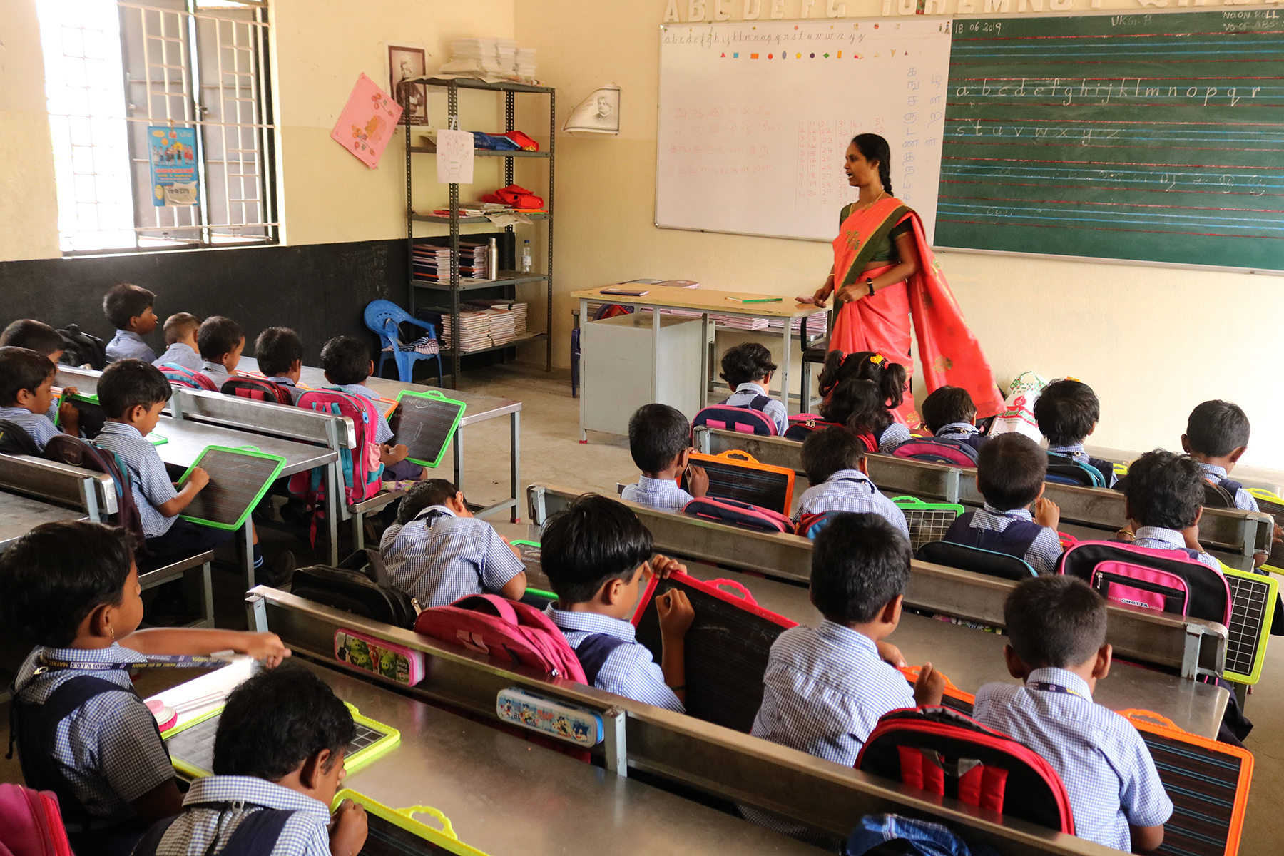 Kinder sitzen im Schulzimmer und werden von einer Lehrerin unterrichtet.
