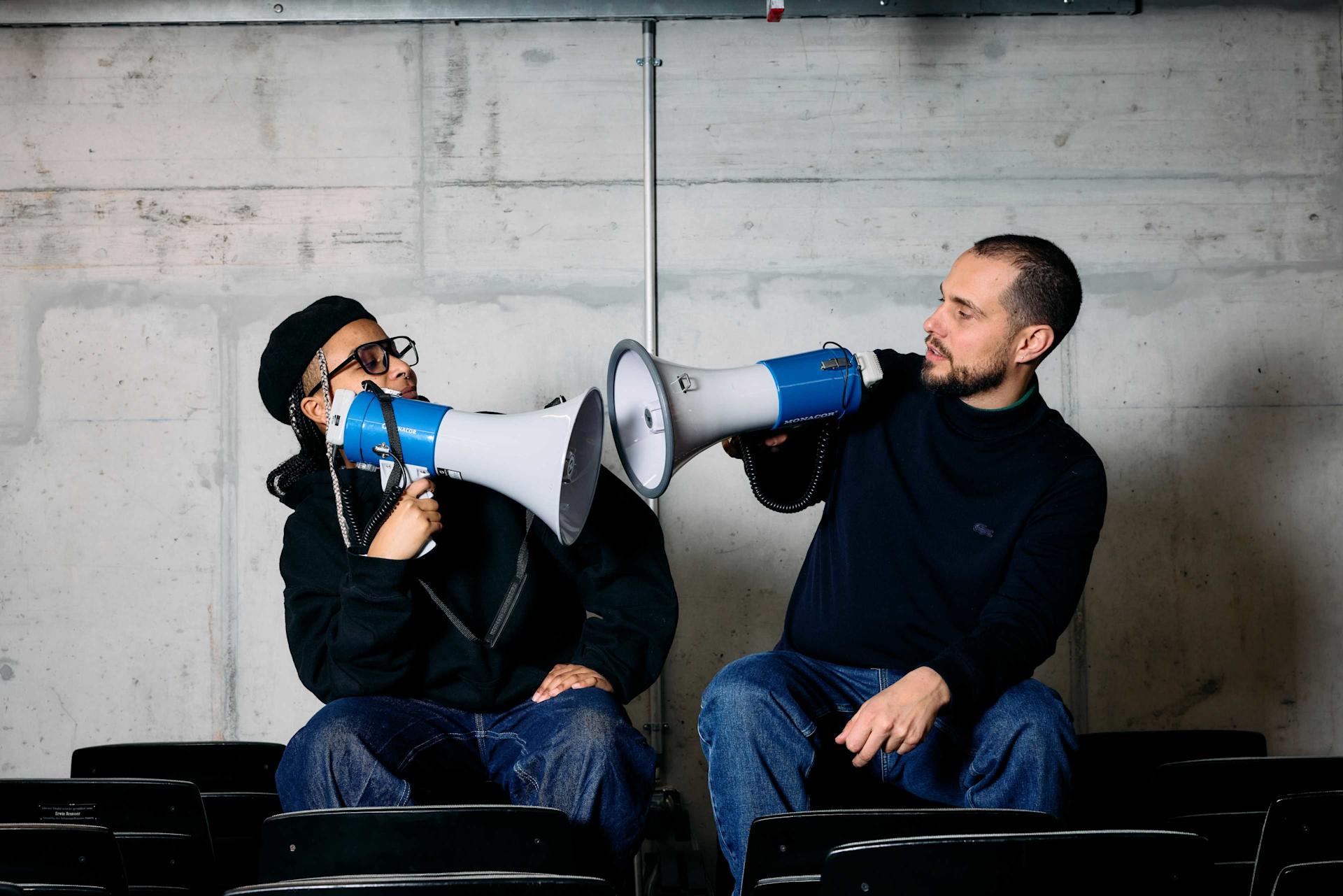 Le rappeur Soukey et Luc de Lo & Leduc sont assis l'un en face de l'autre et tiennent un mégaphone dans leurs mains