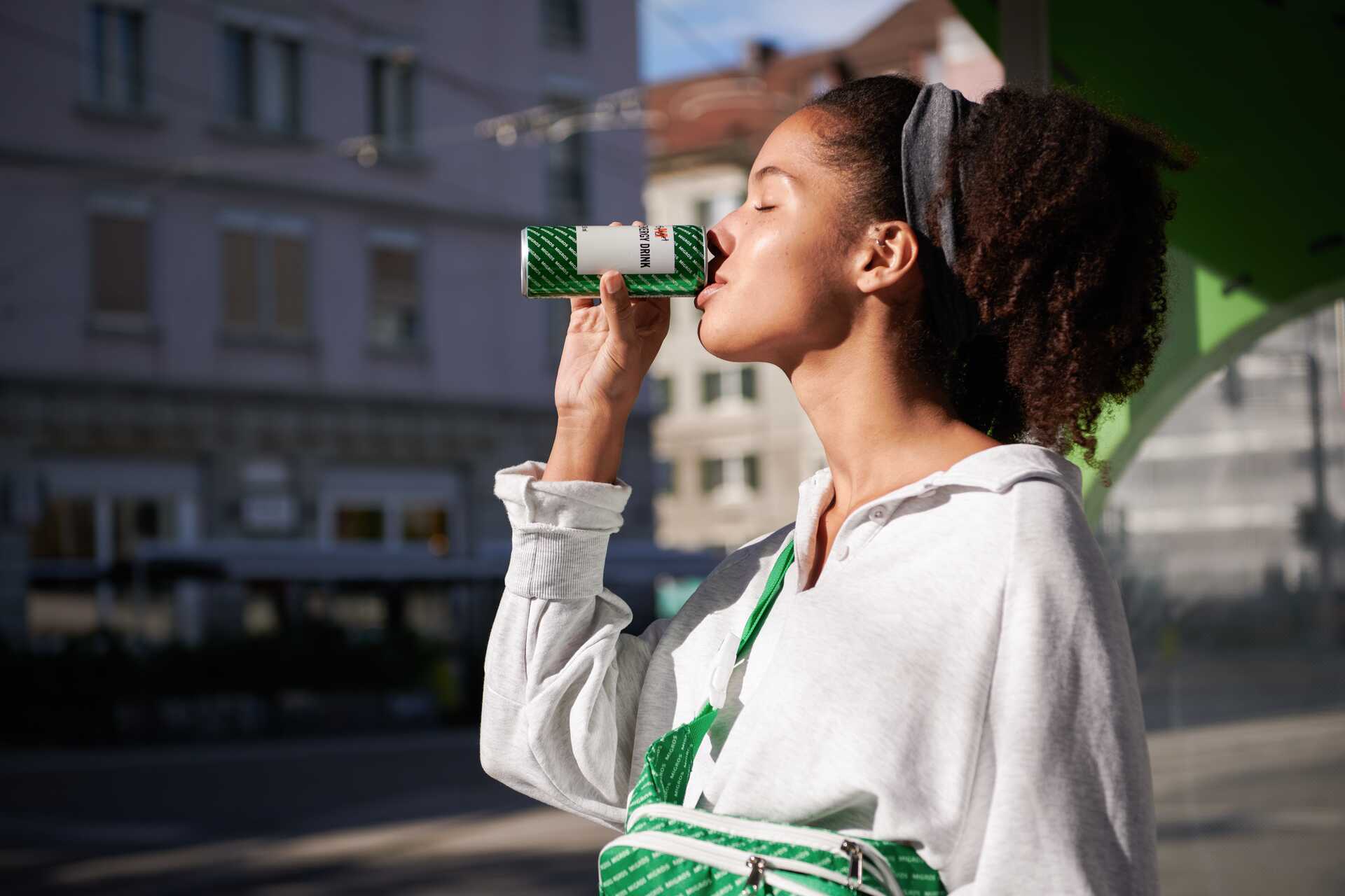 Une jeune femme boit une boisson énergétique M-Budget.
