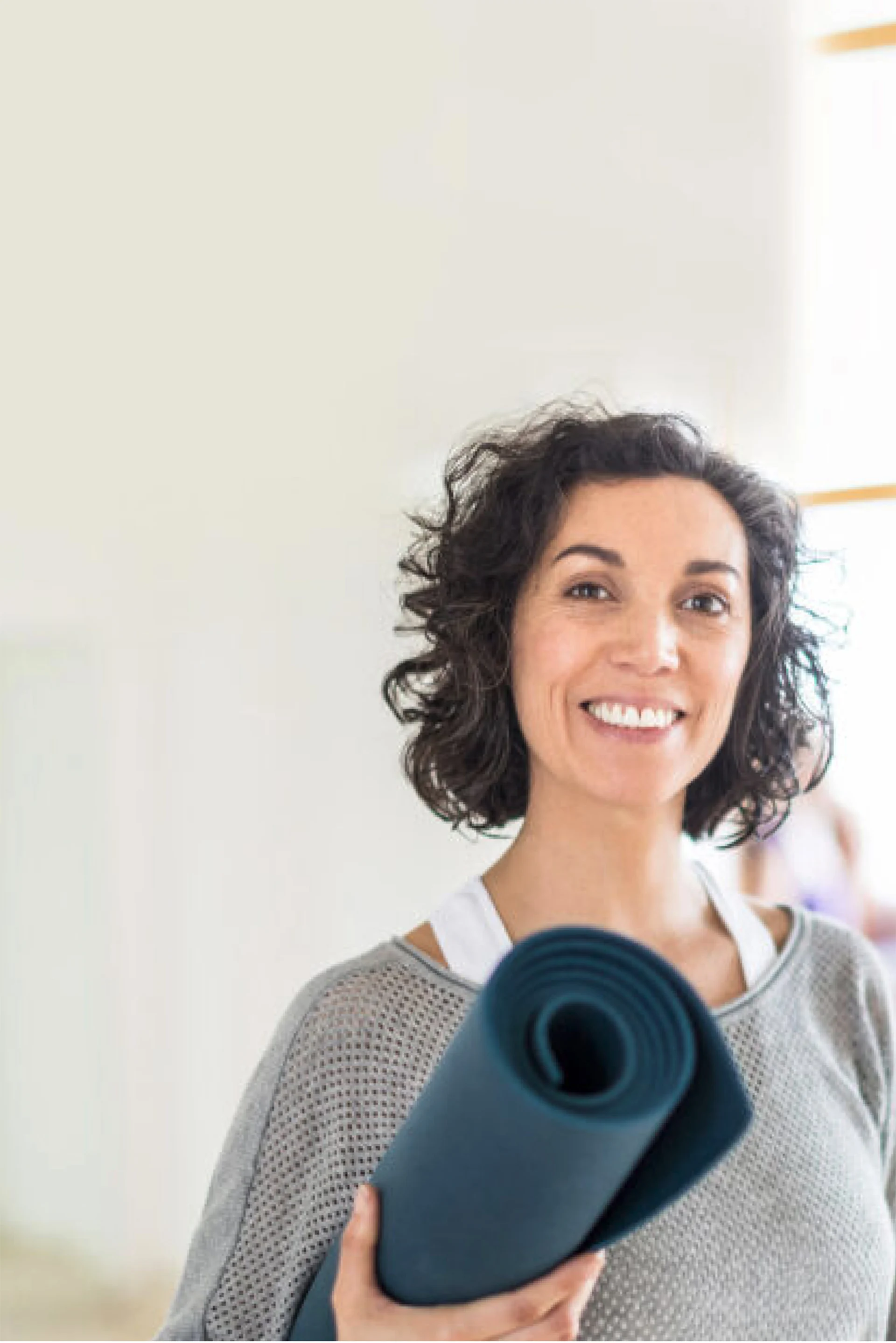 A woman in a yoga studio with a rolled-up yoga mat